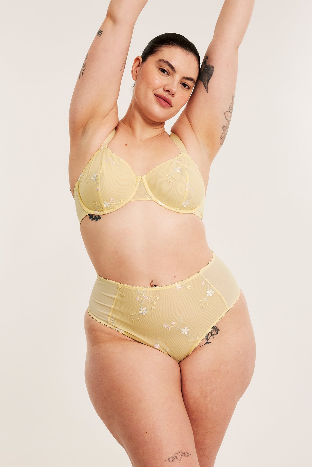 Nainen edestä, yllään vaaleankeltaiset kirjaillut korkeavyötäröiset pikkuhousut ja yhteensopivat rintaliivit.