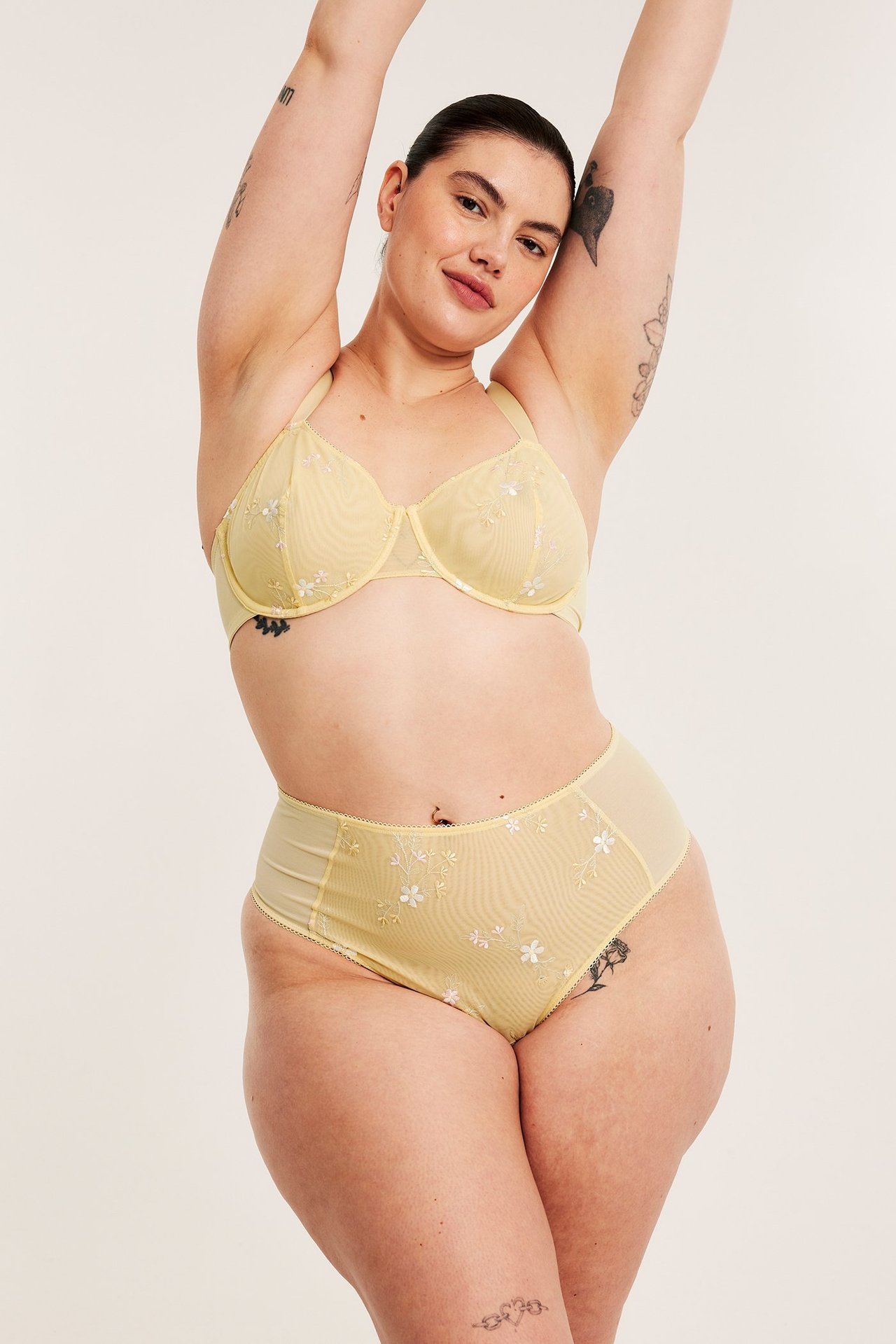 Widok z przodu kobiety w jasnych, żółtych, haftowanych, wysokostanowych figach z siateczki i pasującym biustonoszu.
