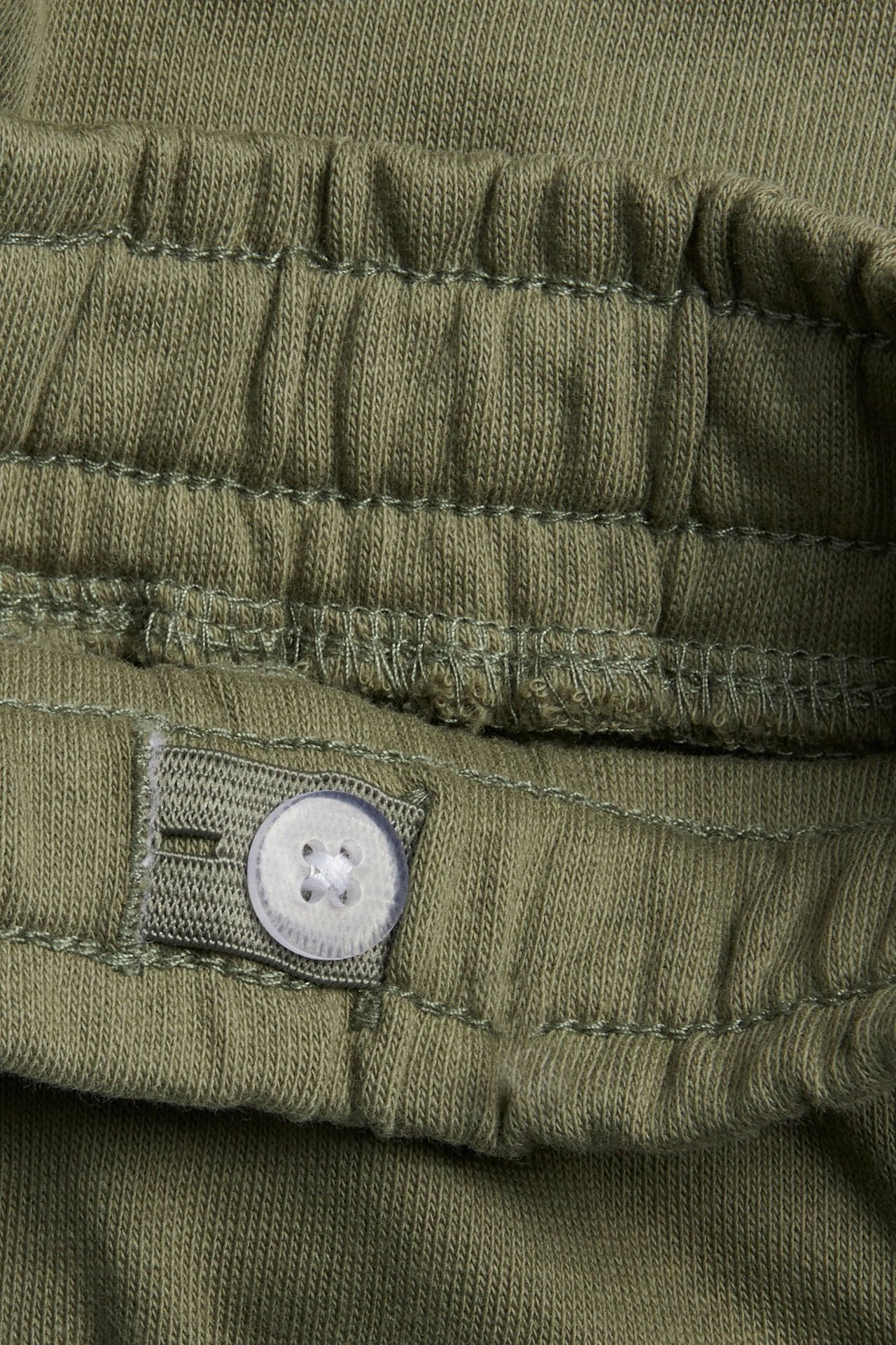 Lähikuva tummanvihreistä puuvillajerseyshortseista, joissa on joustava vyötärö ja säädettävä nappi.