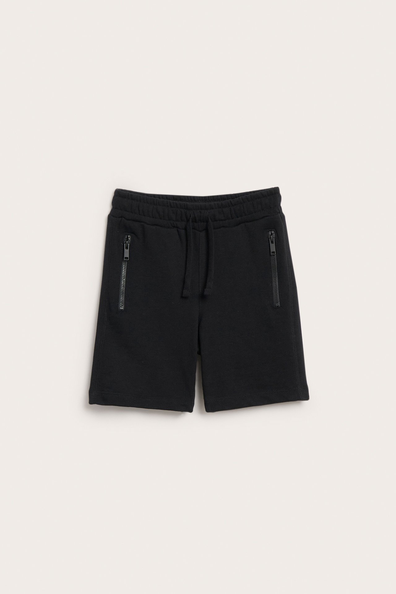 Edestä, mustat lasten puuvillajerseyshortsit vetoketjullisilla taskuilla ja joustavalla kiristysnyörillä varustetulla vyötäröllä.