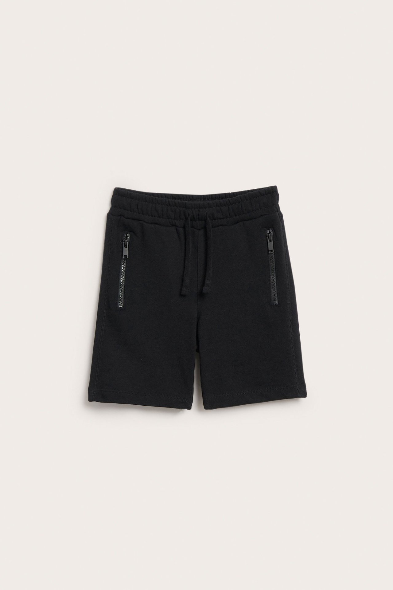 Edestä, mustat lasten puuvillajerseyshortsit vetoketjullisilla taskuilla ja joustavalla kiristysnyörillä varustetulla vyötäröllä.