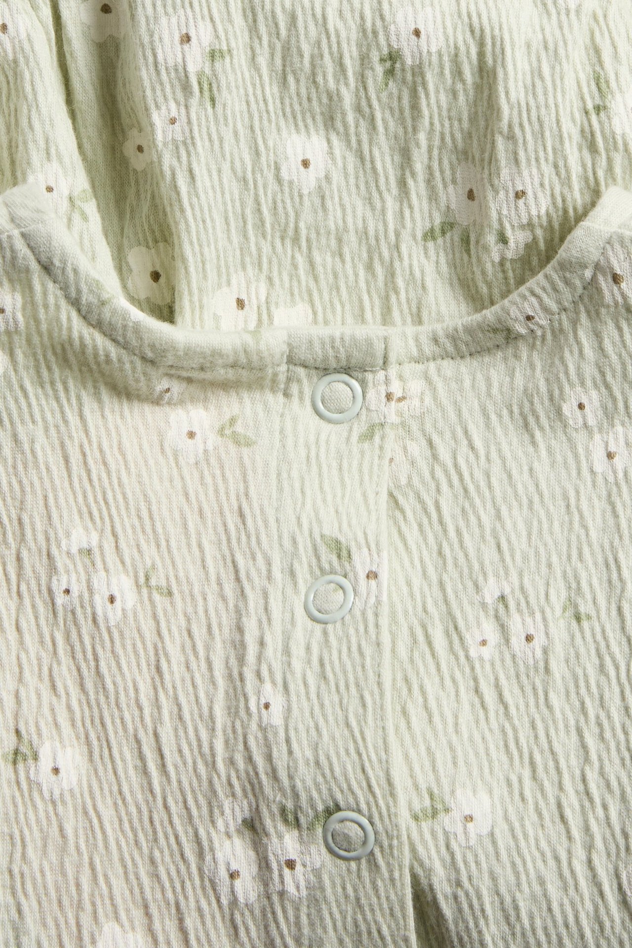 Lähikuva vaaleanvihreästä rypistetystä vauvan kukkakuvioisesta romperista, painonapeilla.