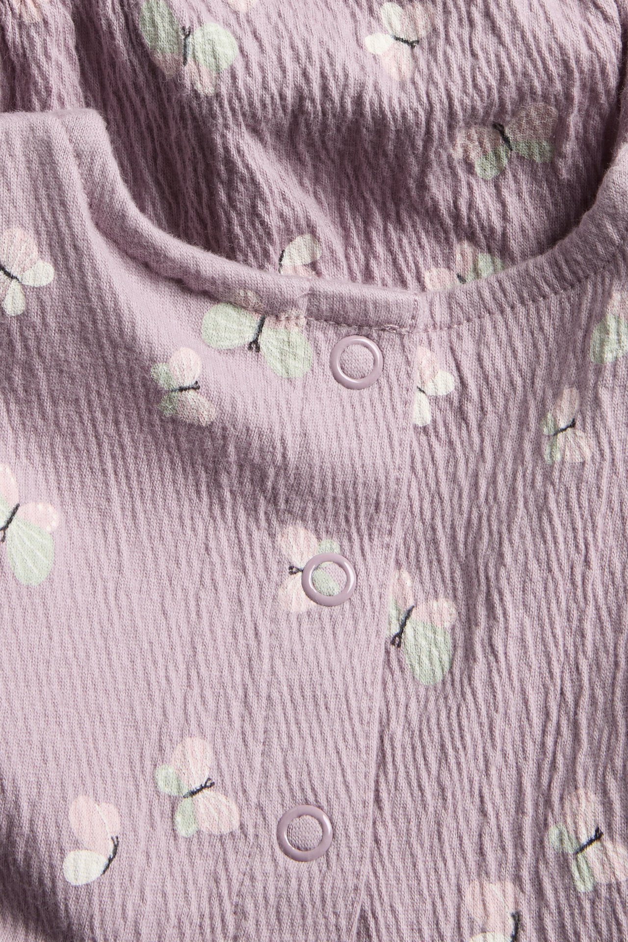 Widok z przodu: Liliowy, teksturowany pajacyk niemowlęcy z wzorem motyli i zatrzaskami.