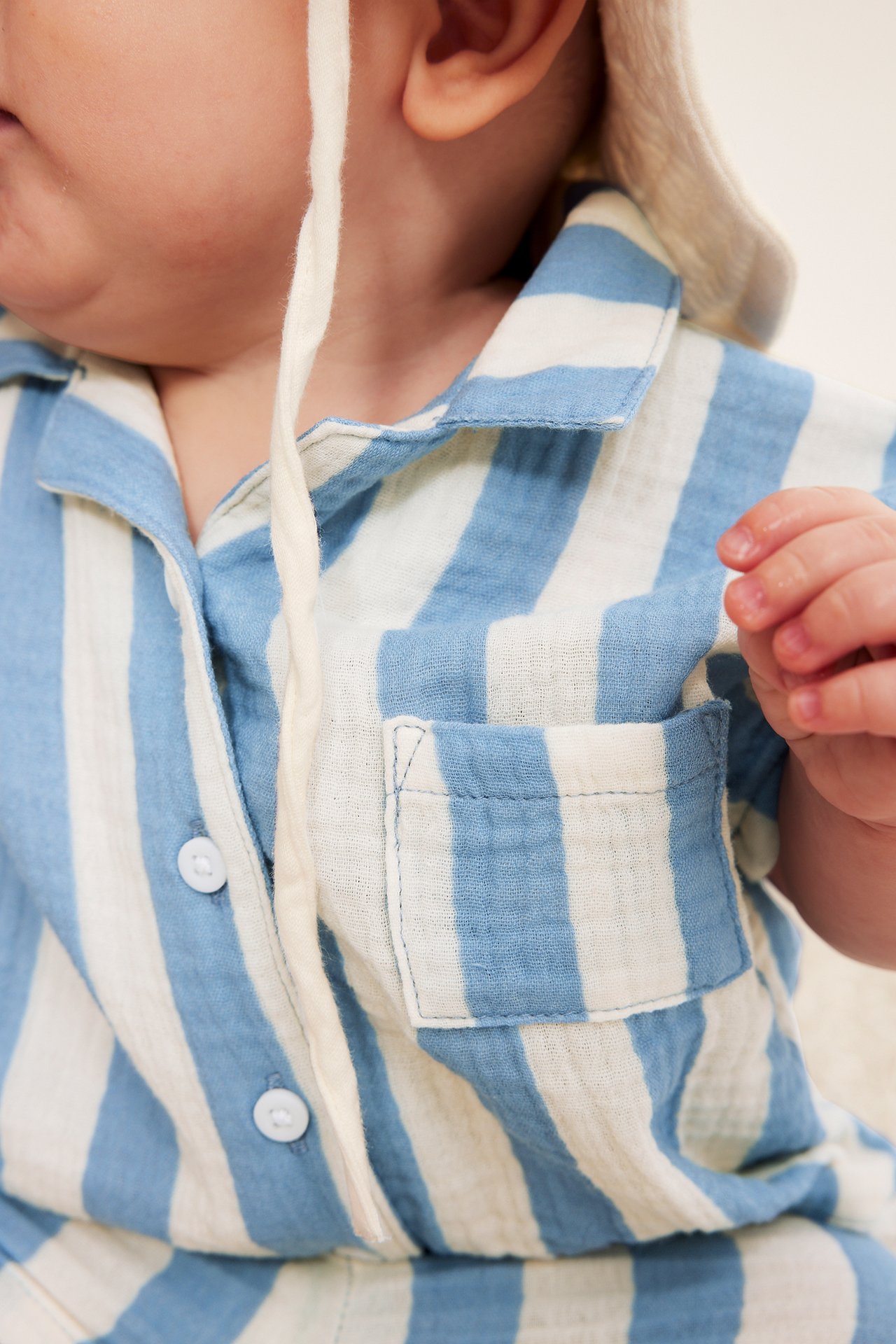 Närbild på en baby i en ljusblå och vitrandig skjorta i muslin med bröstficka.