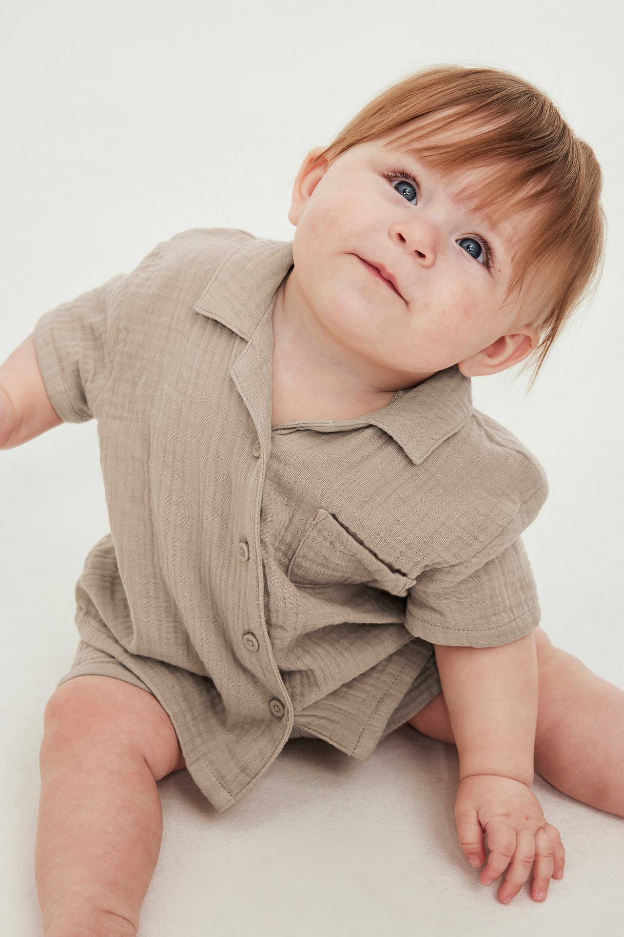 Frontvisning av baby i beige kortermet musselinskjorte med brystlomme og matchende shorts.