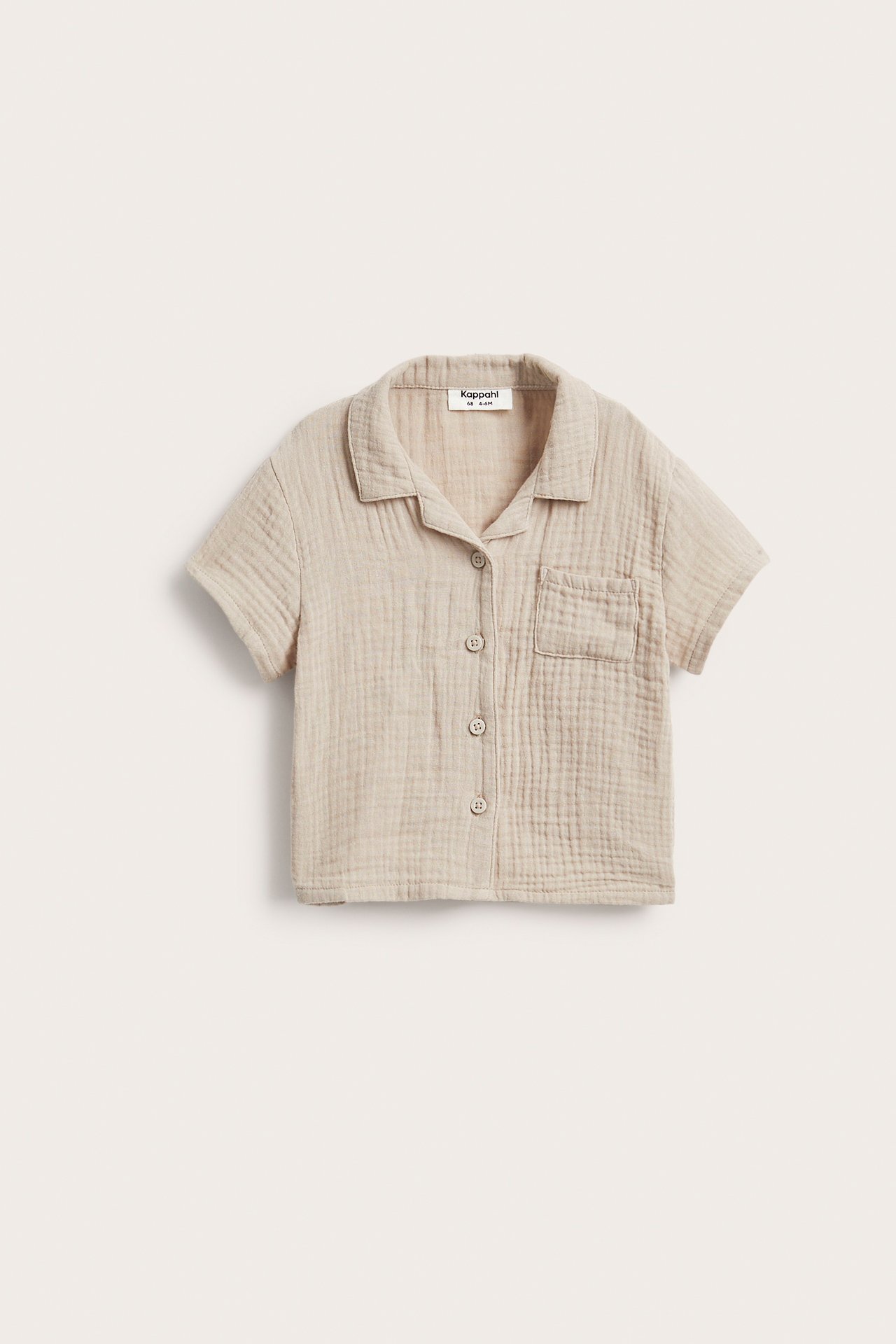 Edestä näkymä beigestä lyhythihaisesta musliinipaidasta, jossa kaulus, nappikiinnitys ja rintatasku.