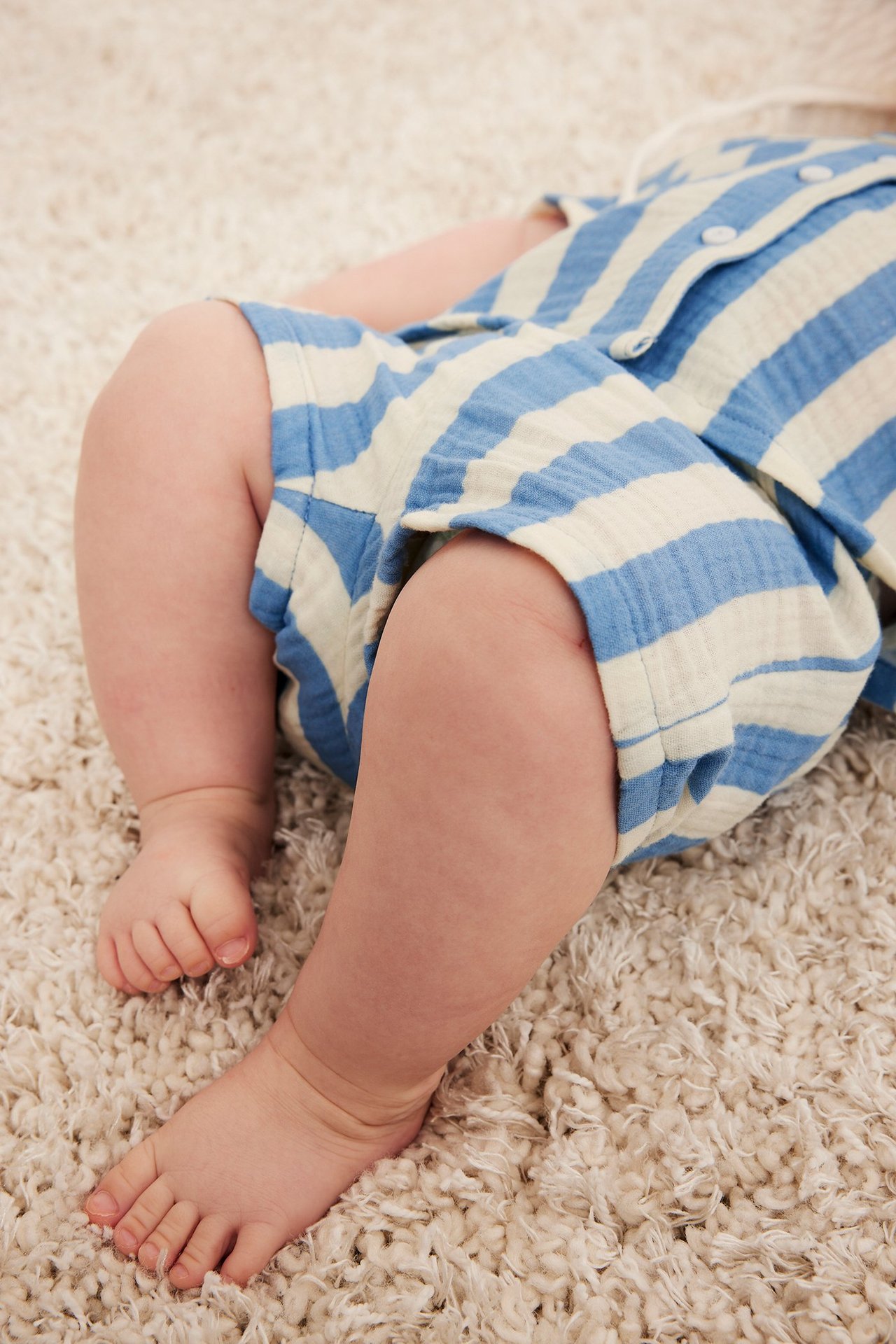 Närbild på en baby i ljusblå- och vitrandiga muslinshorts och en matchande topp.