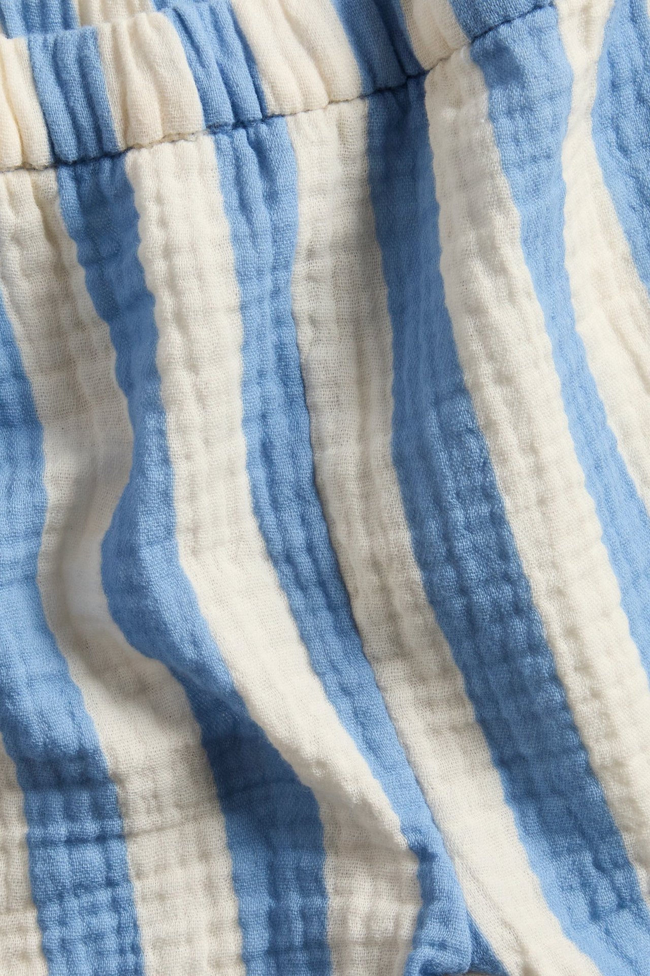 Nærbilde av lyseblå og kremhvite stripete musselinshorts med elastisk midje.