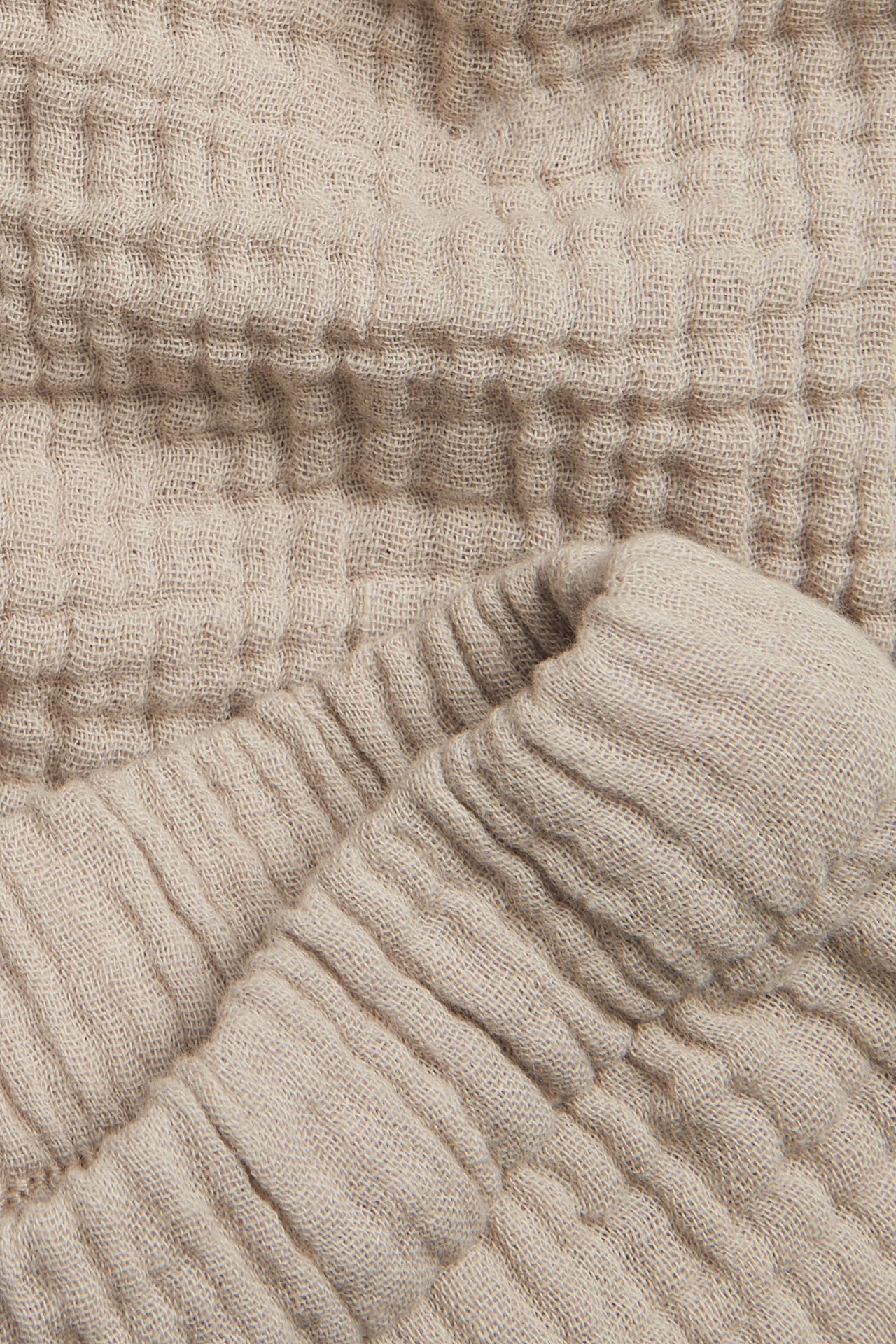 Lähikuva beigestä musliinishortsista, jossa joustava vyötärö, näyttäen kuvioidun puuvillakankaan.