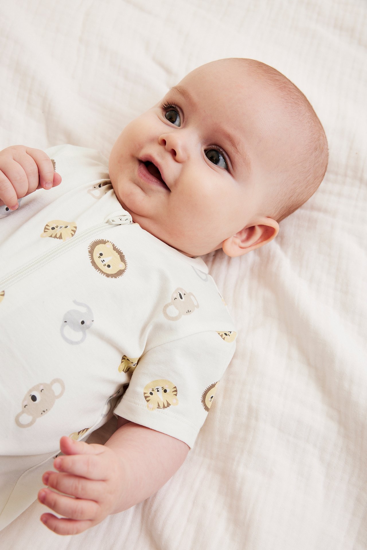 Nærbilde av baby i en kortermet offwhite romper med dyremønster og glidelås foran.
