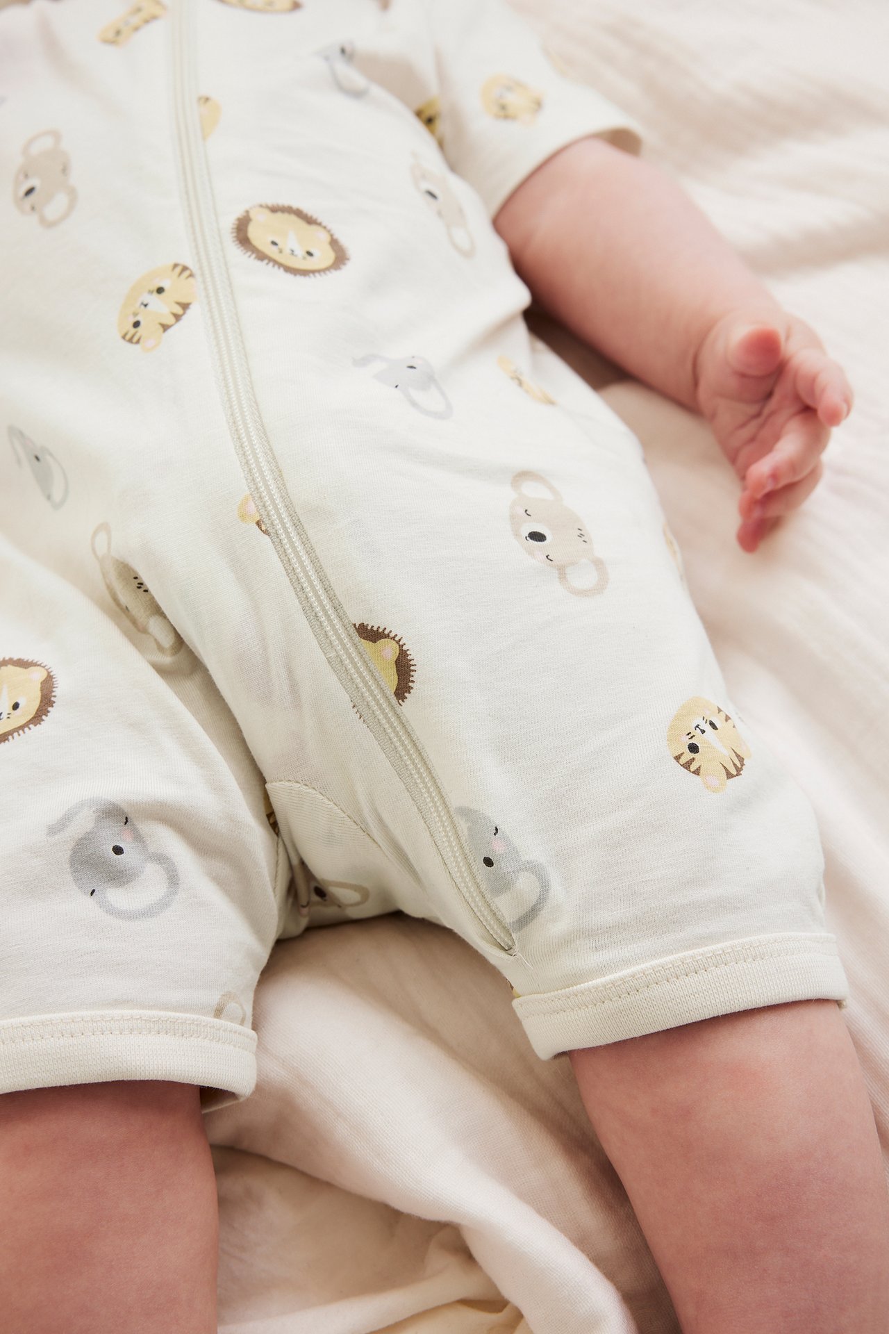 Nærbilde av baby i offwhite kortermet romper med dyremønster og glidelås foran.