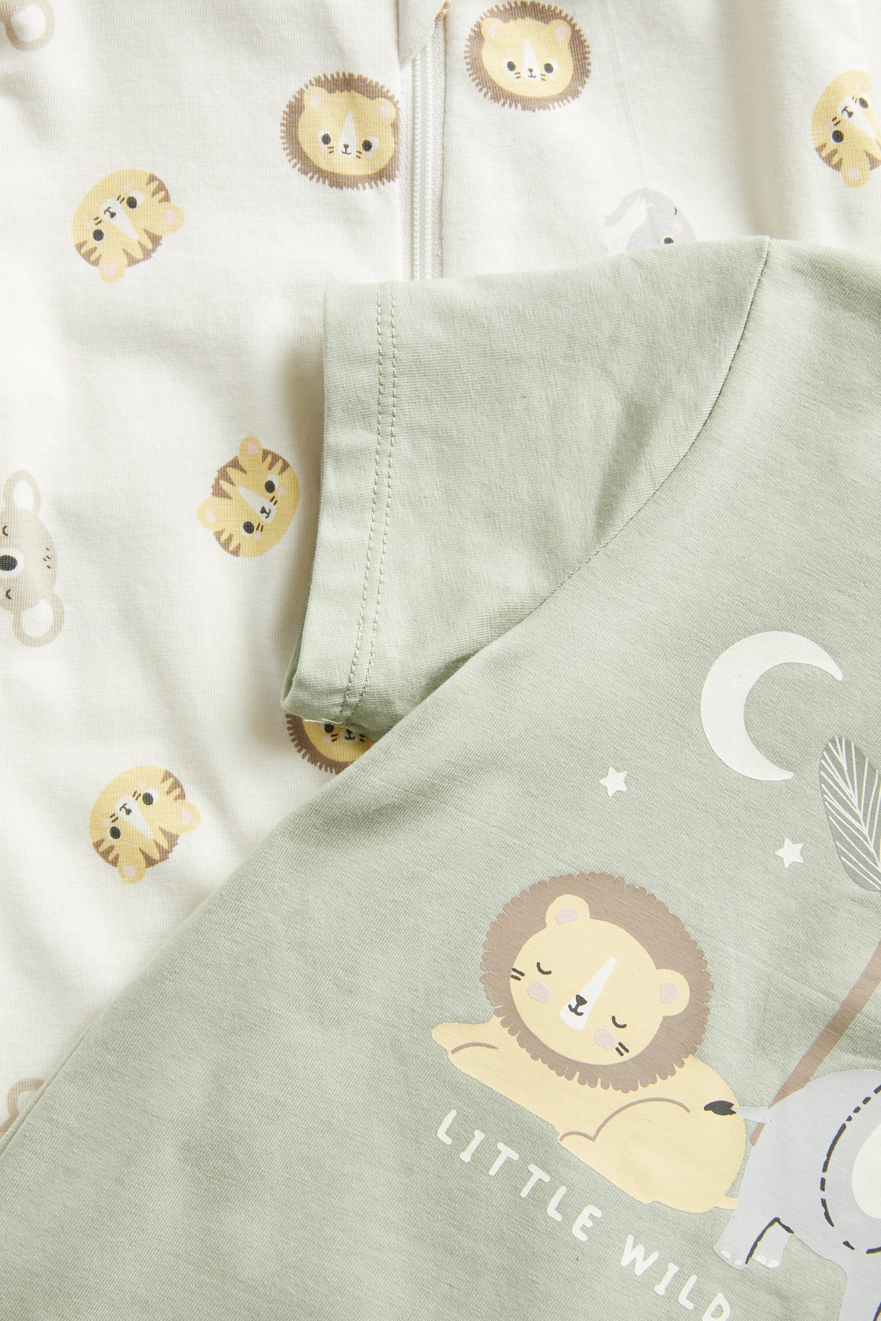 Nærbilde av en lysegrønn babyromper med løvemønster og en off-white romper med dyremønster og glidelås.