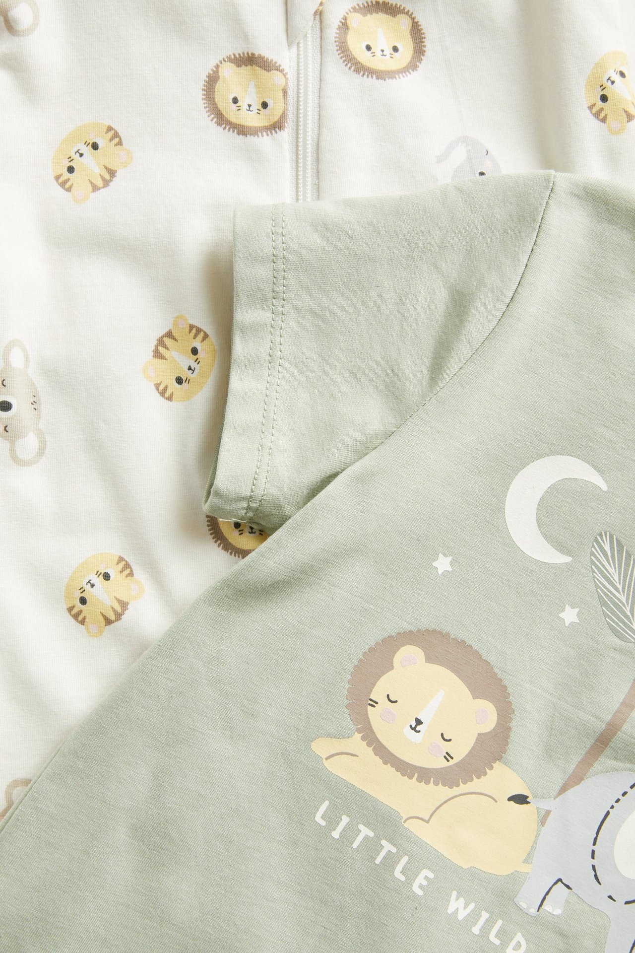 Zbliżenie na jasnozielony pajac niemowlęcy z nadrukiem lwa oraz ecru pajac w zwierzęta z zamkiem błyskawicznym.