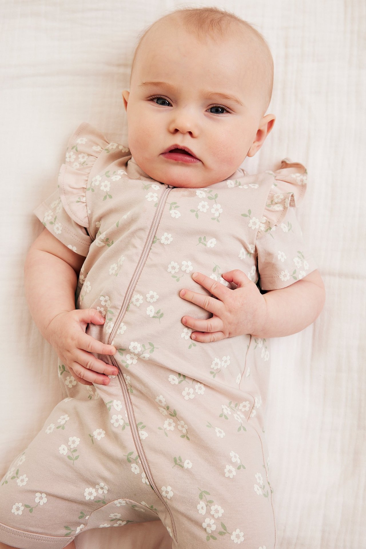 Övervy av ett baby i en rosa blommig kortärmad romper med volanger och dragkedja fram.