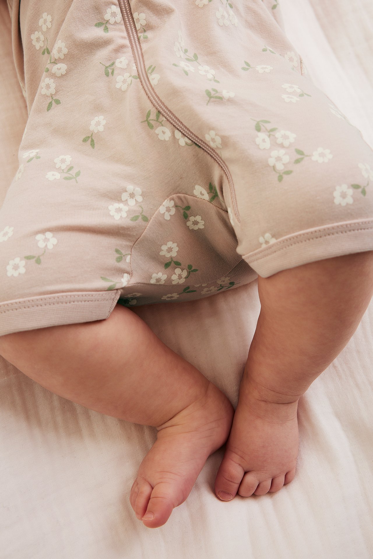 Närbild på baby i rosa kortärmad romper med vitt blommönster och dragkedja.