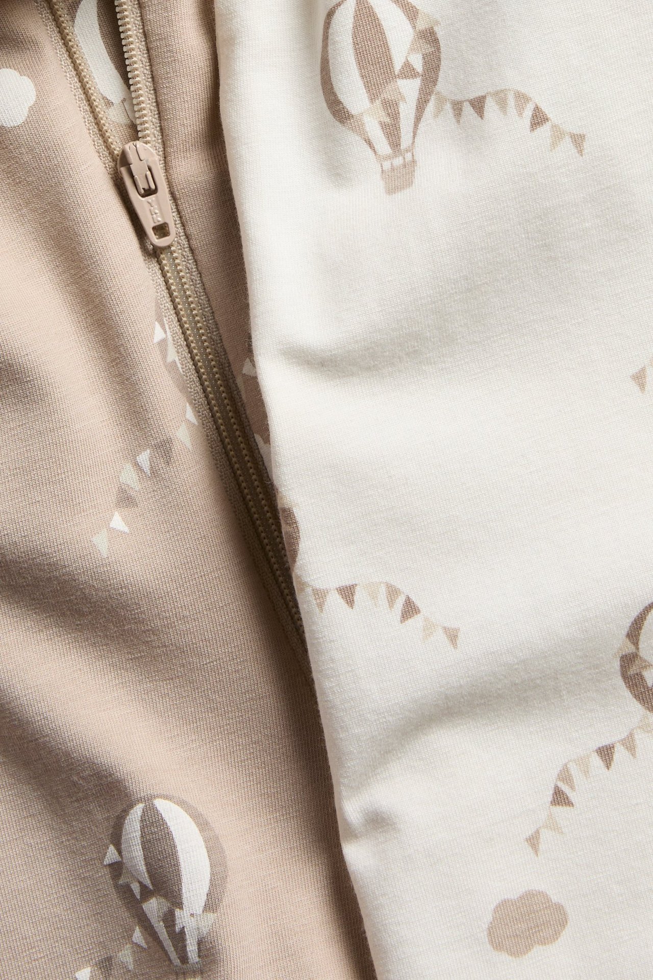 Lähikuva vauvanpotkupuvuista: vaaleanruskea ja luonnonvalkoinen, ilmalaivakuvioitu, vetoketjulla.