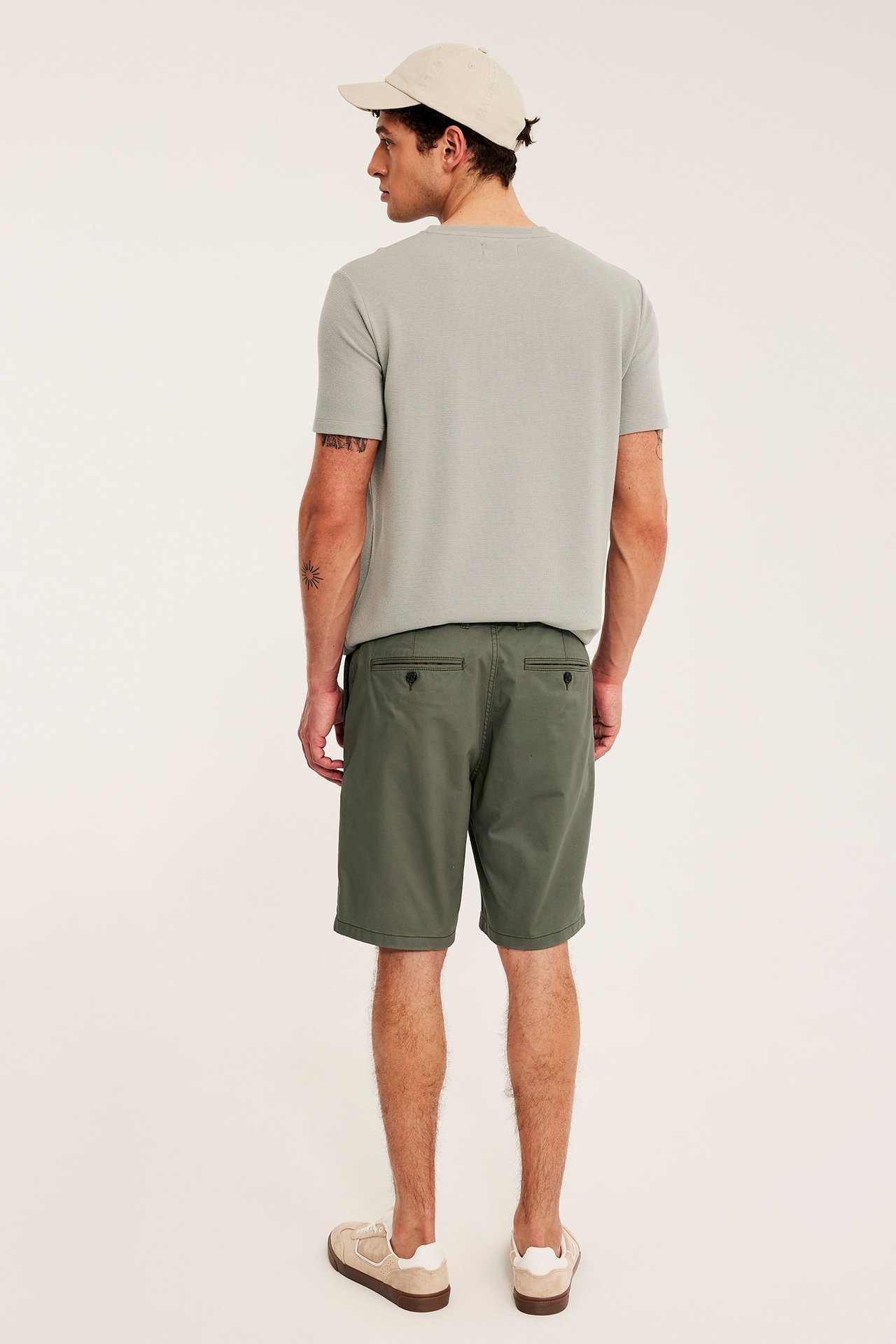 Bakfra: Mann i grønne chino-shorts, lys grønn t-skjorte, beige caps og joggesko.
