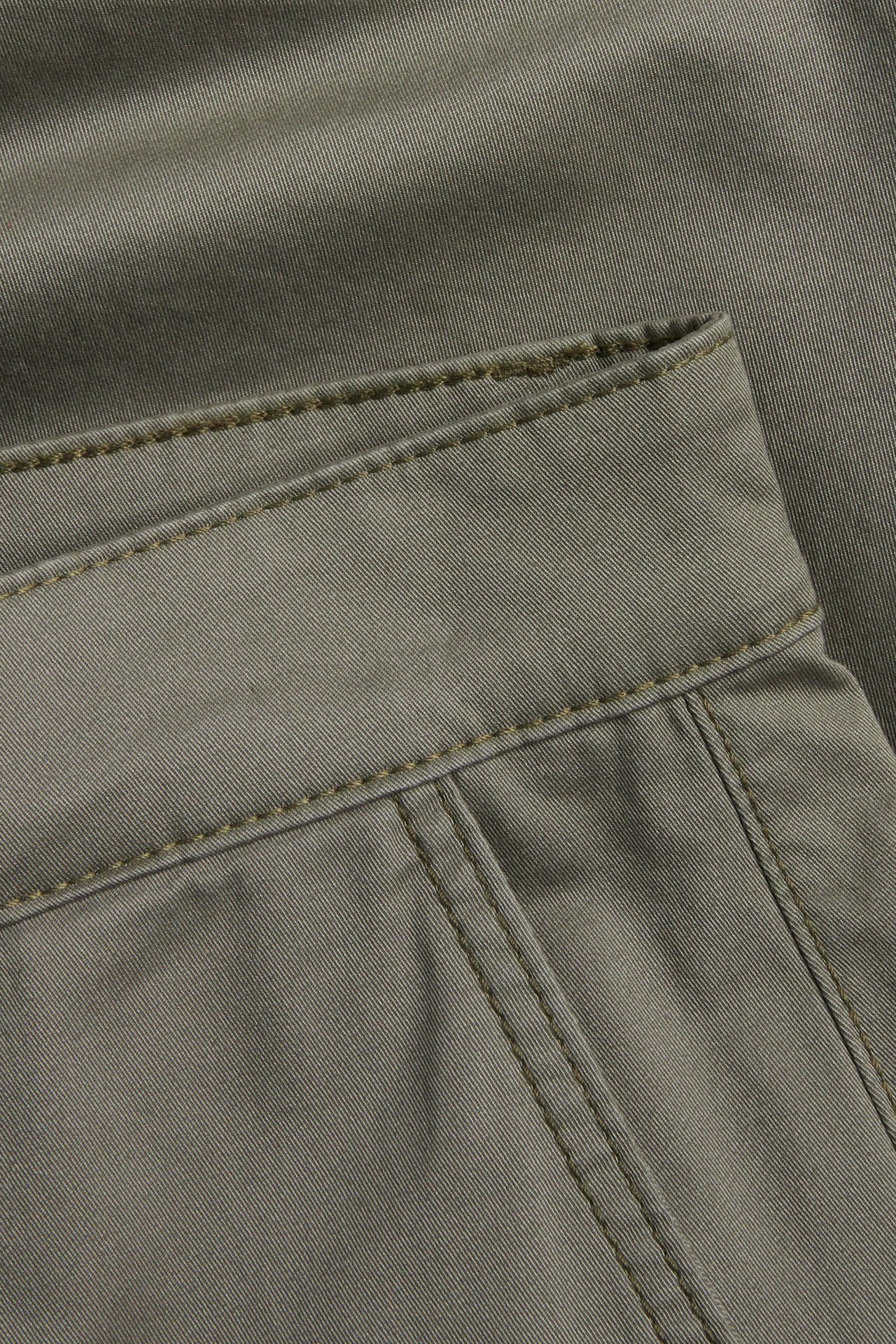 Närbild på midjebandet av gröna bomullstwill chinosshorts med synliga sömmar.