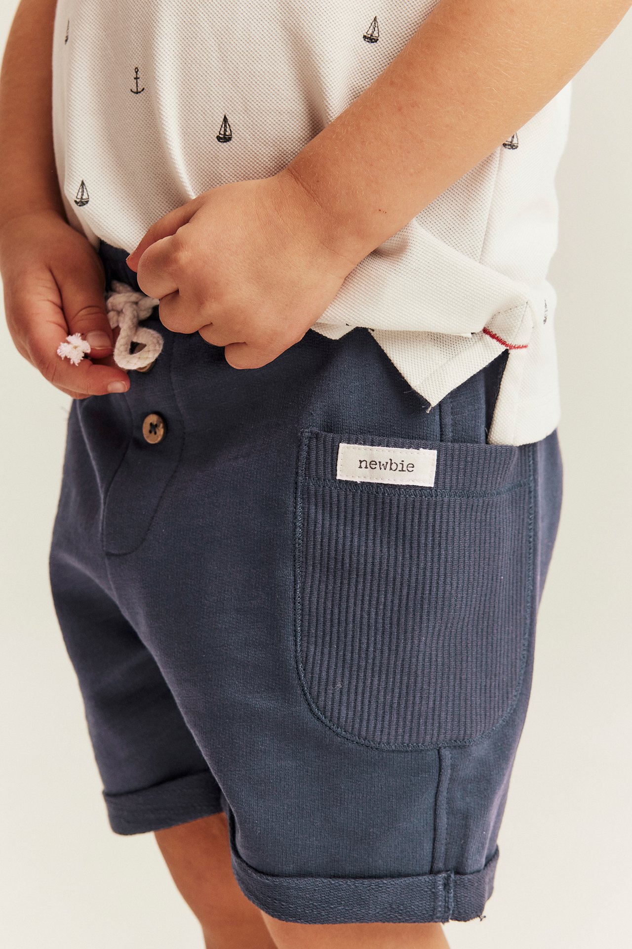 Lähikuva lapsesta tummansinisissä shortsissa, käännetyt lahkeet, ja valkoinen kuvioitu pikeepaita.