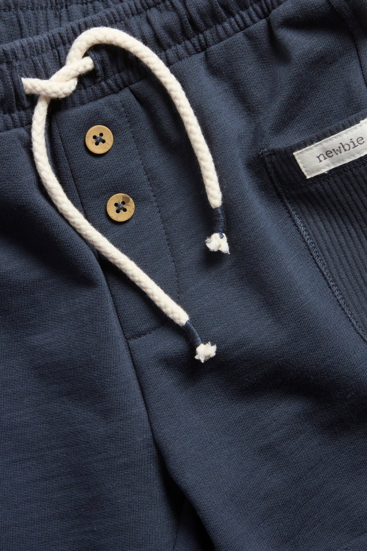 Närbild av mörkblå slubtrikåshorts med resår, vit dragsko, dekorativa knappar och ribbad ficka.