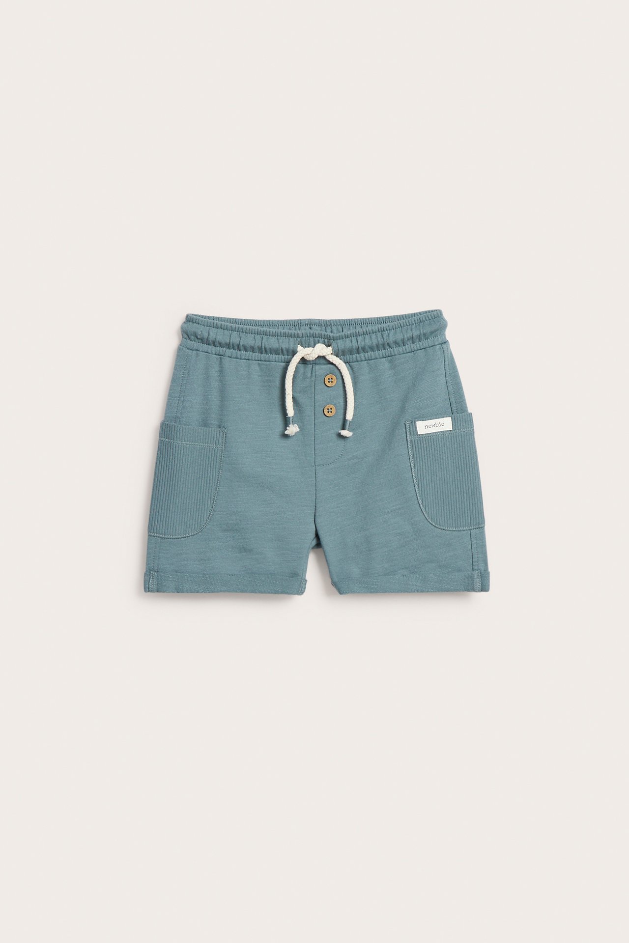 Framifrån: Mörkturkosa barnshorts i slubtrikå med ribbade sidfickor, upprullade benslut och dekorativa knappar.