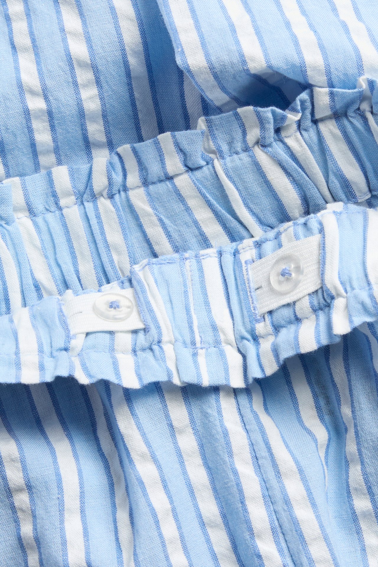 Zbliżenie na dziecięce, niebiesko-białe bawełniane spodnie w paski z elastycznym pasem na guziki.