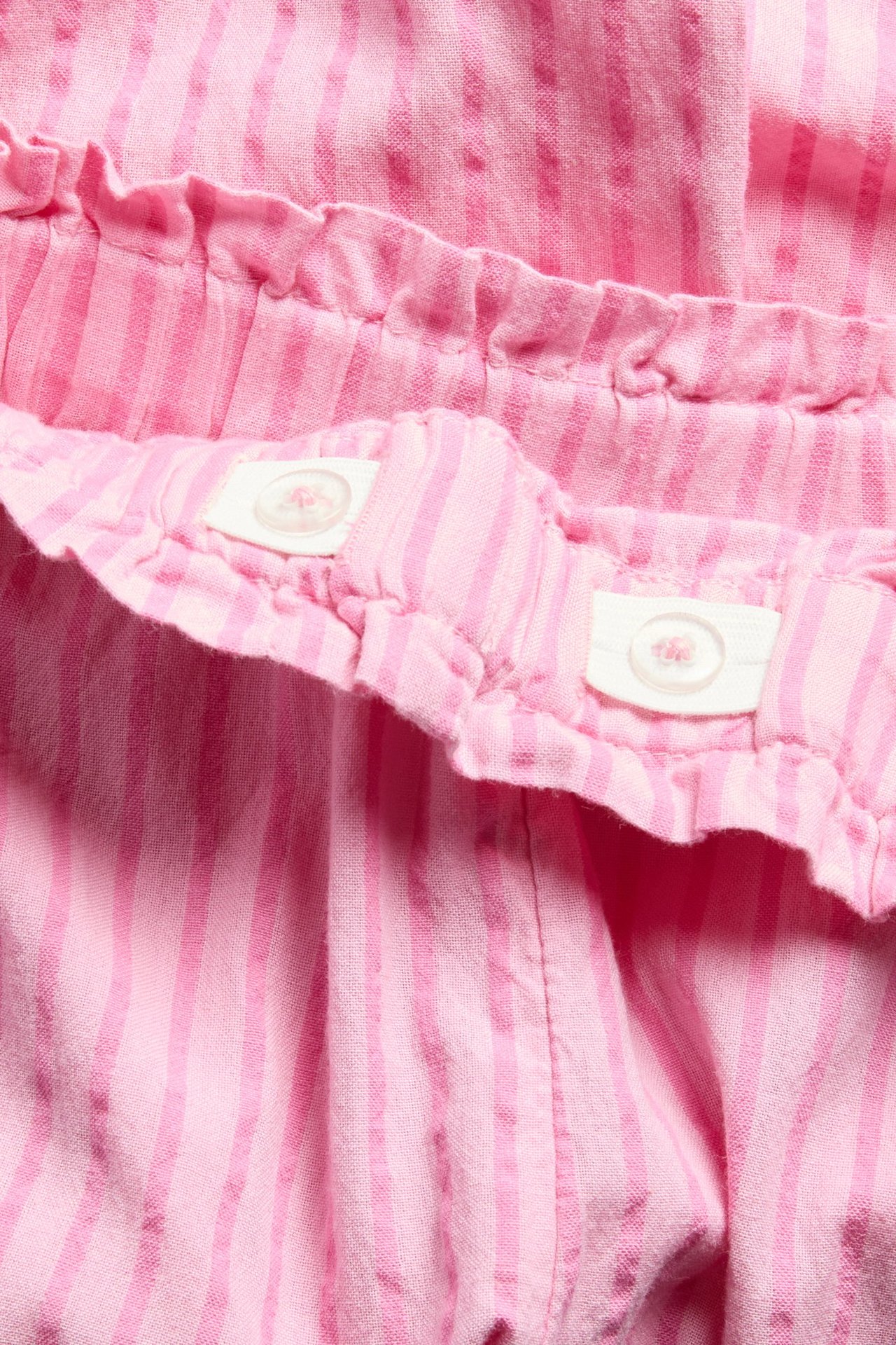 Lähikuva vaaleanpunaisista raidallisista puuvillahousuista säädettävällä napitettavalla vyötäröllä.