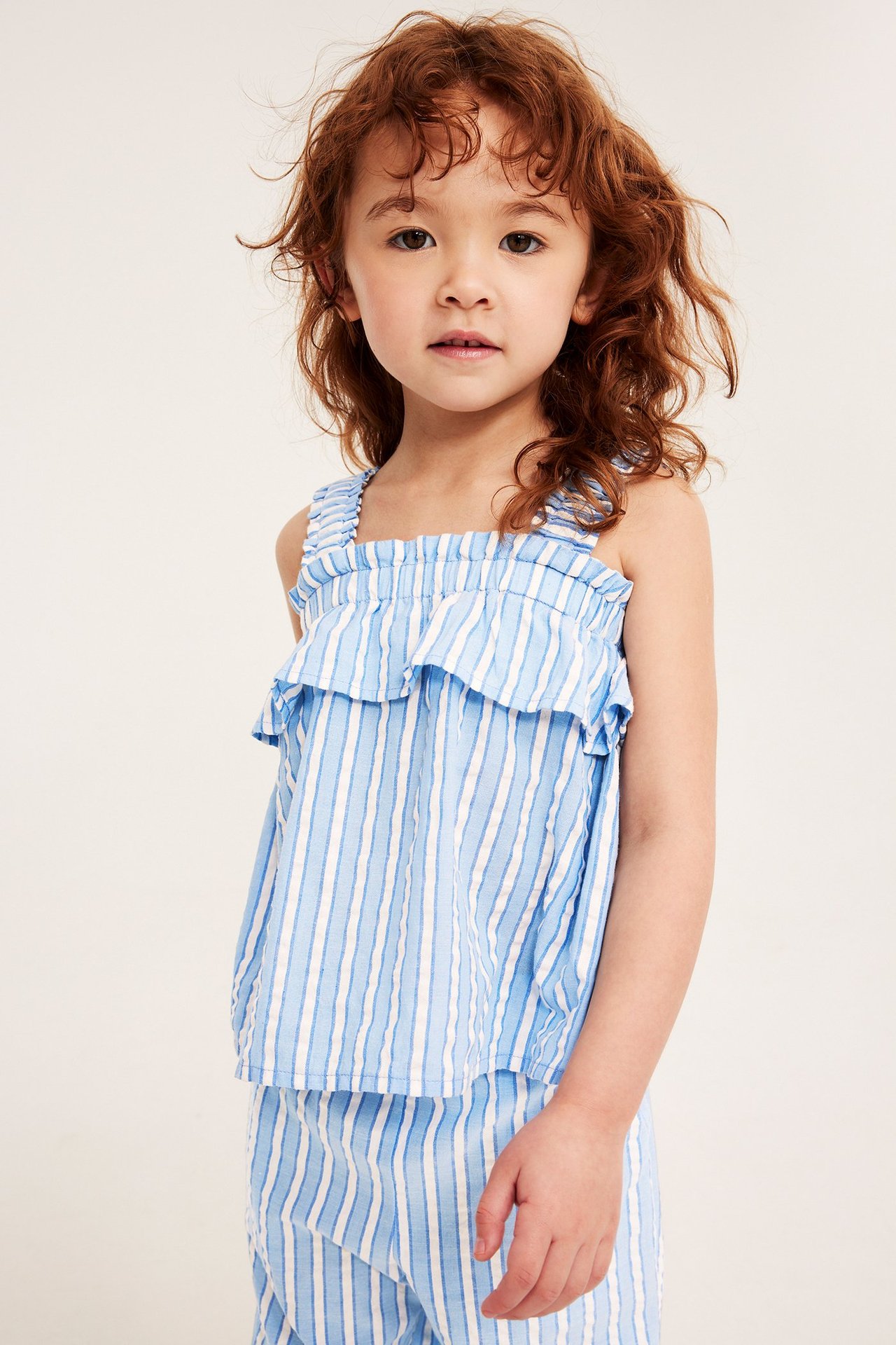 Edestä, lapsi yllään sinivalkoraidallinen puuvillatoppi röyhelöillä ja yhteensopivat housut.