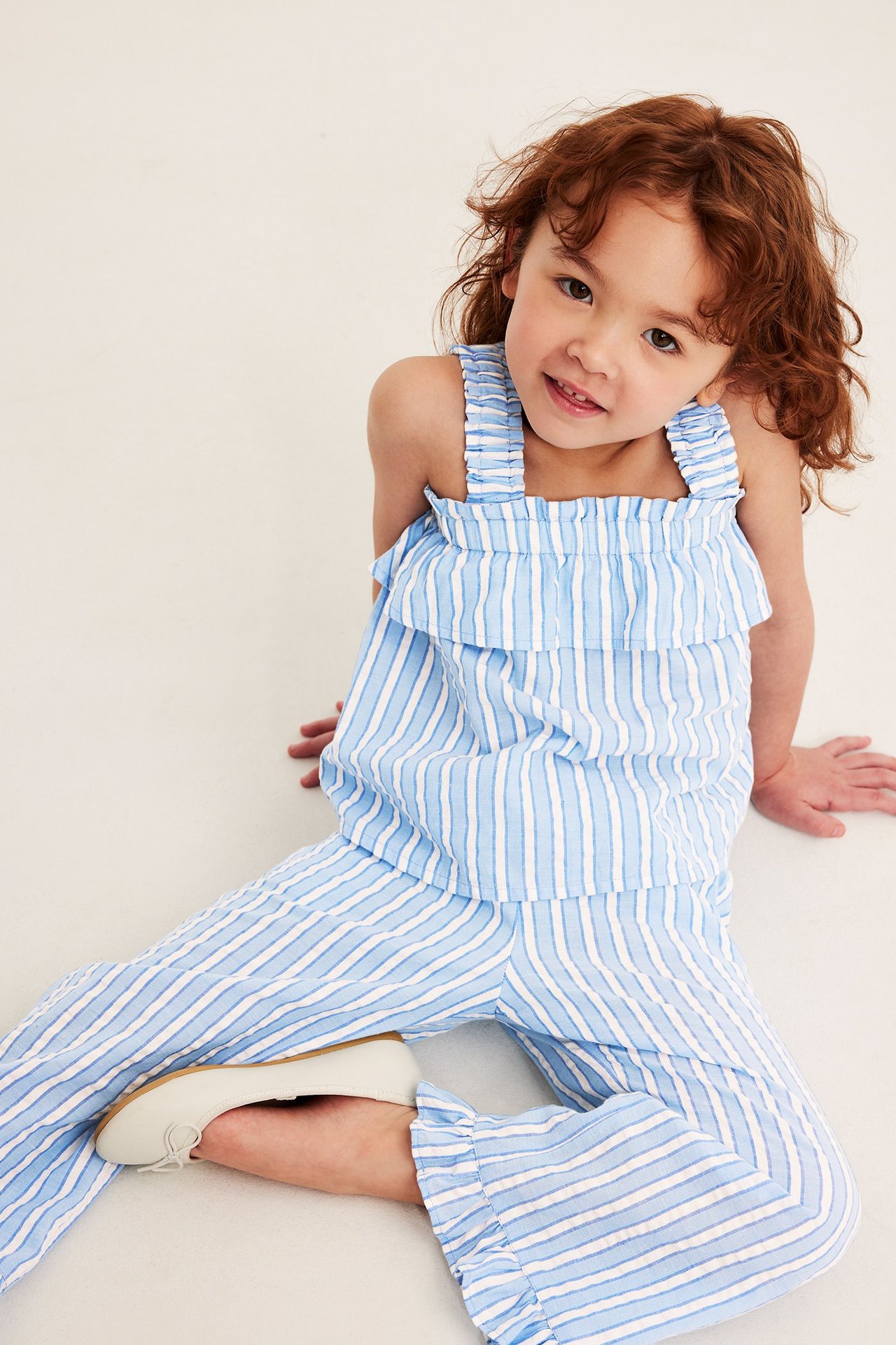 Edestä: Lapsi yllään sinivalkoraidallinen vohvelikankainen kerrospaita, yhteensopivat housut ja valkoiset ballerinat.