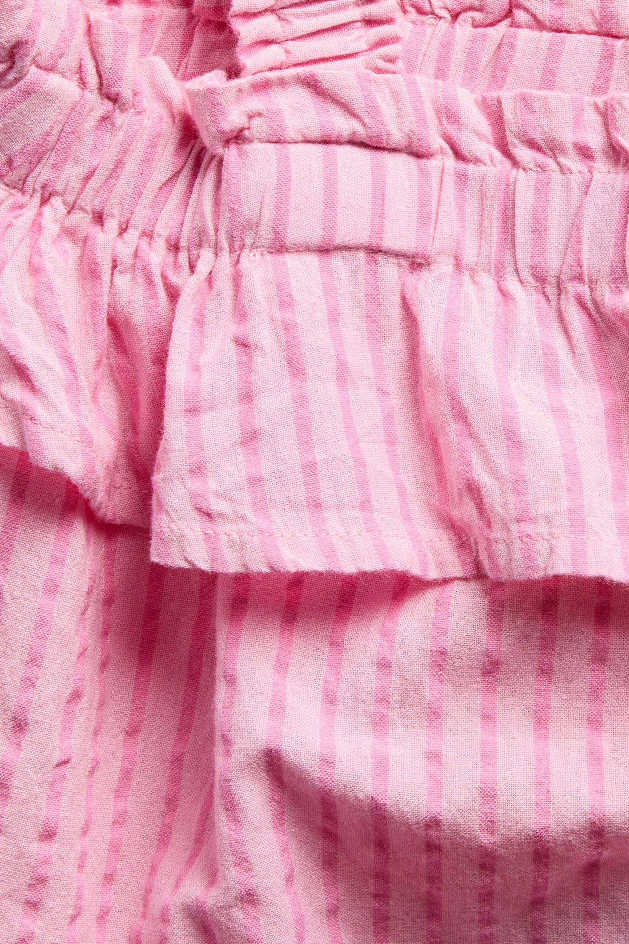 Zbliżenie różowego bawełnianego topu w paski z falbanami.