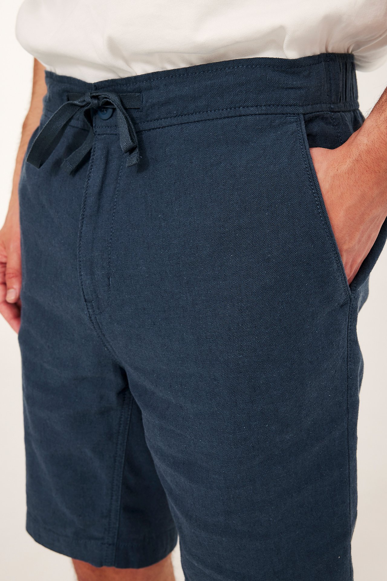 Zbliżenie na mężczyznę w ciemnoniebieskich szortach z mieszanki lnu, ze sznurkiem i ręką w kieszeni.