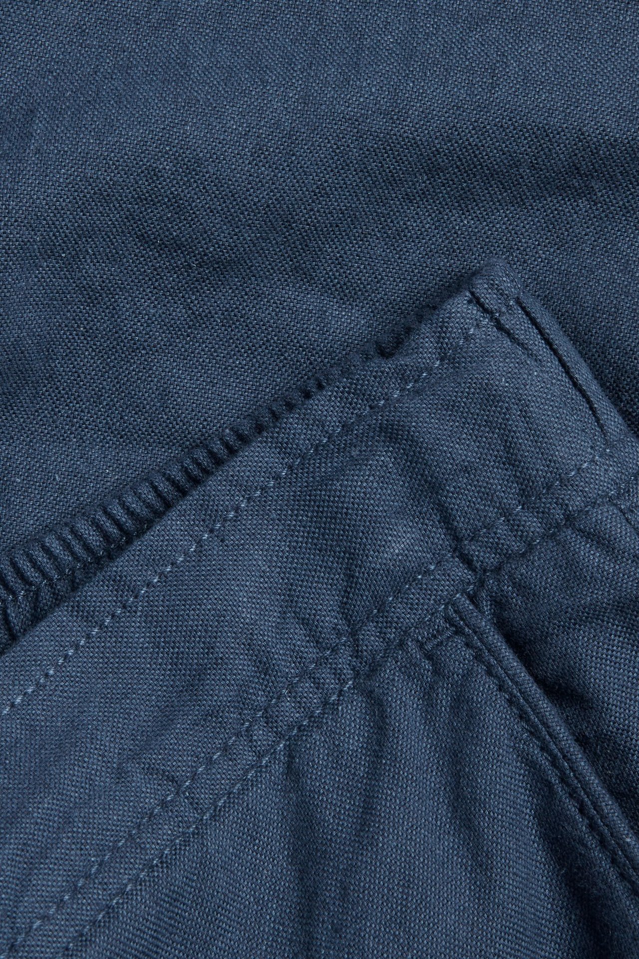 Närbild på mörkblå linneblandningsshorts, visar tygets struktur, sömmar och resår i midjan.