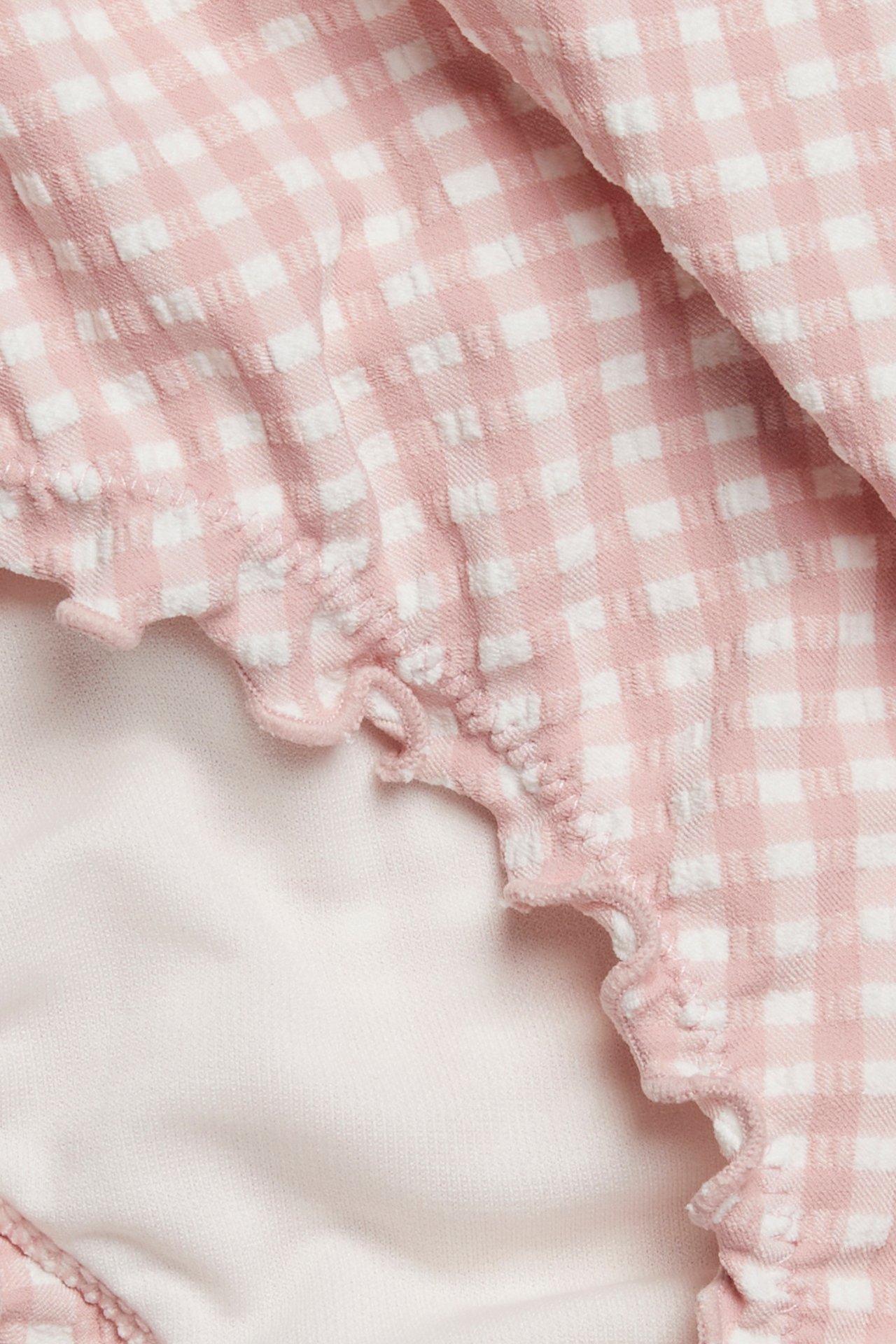 Zbliżenie różowo-białych, kraciastych fig bikini z falbanką i jasnoróżową podszewką.