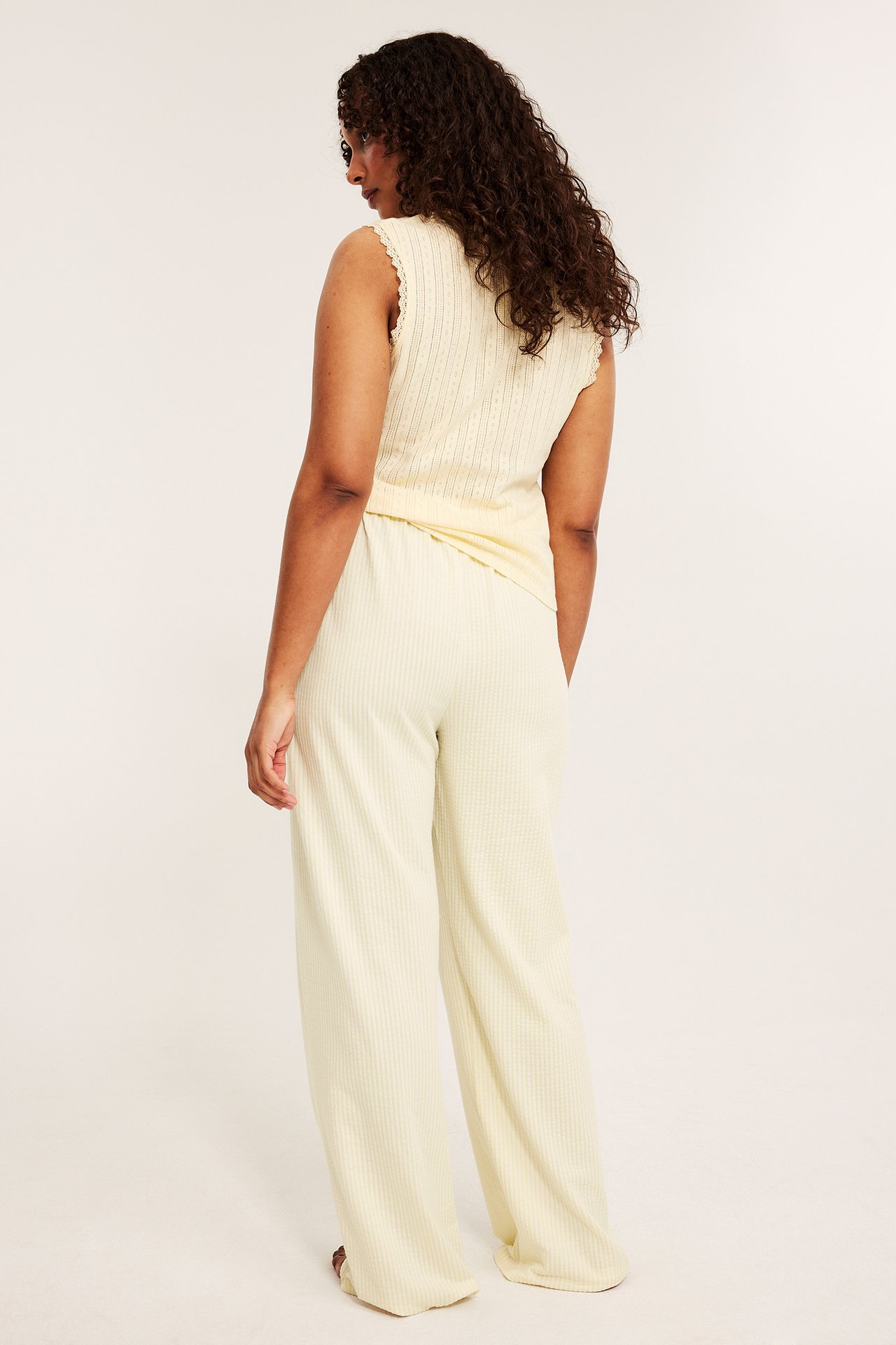 Kvinna bakifrån i ljusgula pyjamasbyxor med bäckebölja-struktur, resårmidja och matchande ärmlös topp.