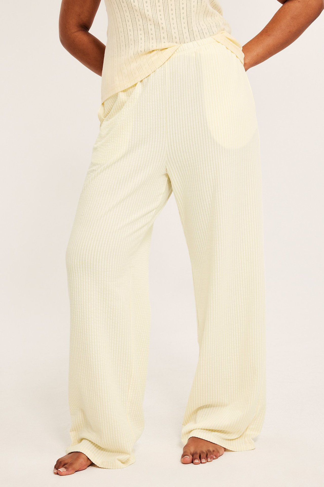 Edestä kuvattu nainen yllään vaaleankeltaiset rypytetyt leveälahkeiset pyjamahousut ja yhteensopiva toppi.