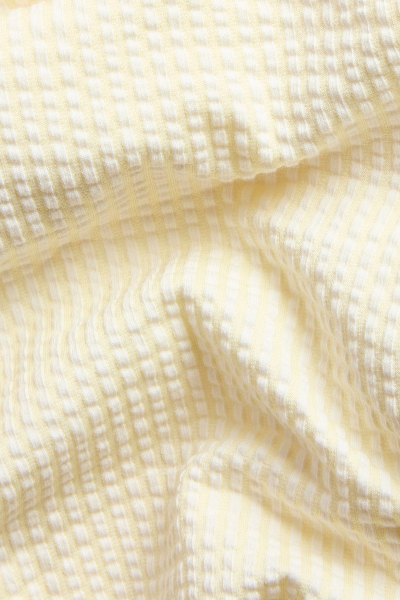 Zbliżenie na jasnożółte, paski, rypsowe spodenki piżamowe z teksturowaną powierzchnią.