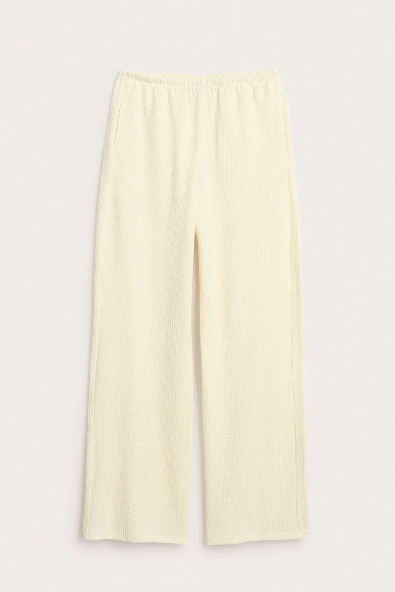 Widok z przodu jasne, żółte, szerokie spodnie piżamowe z teksturą seersucker, elastycznym pasem i kieszeniami.