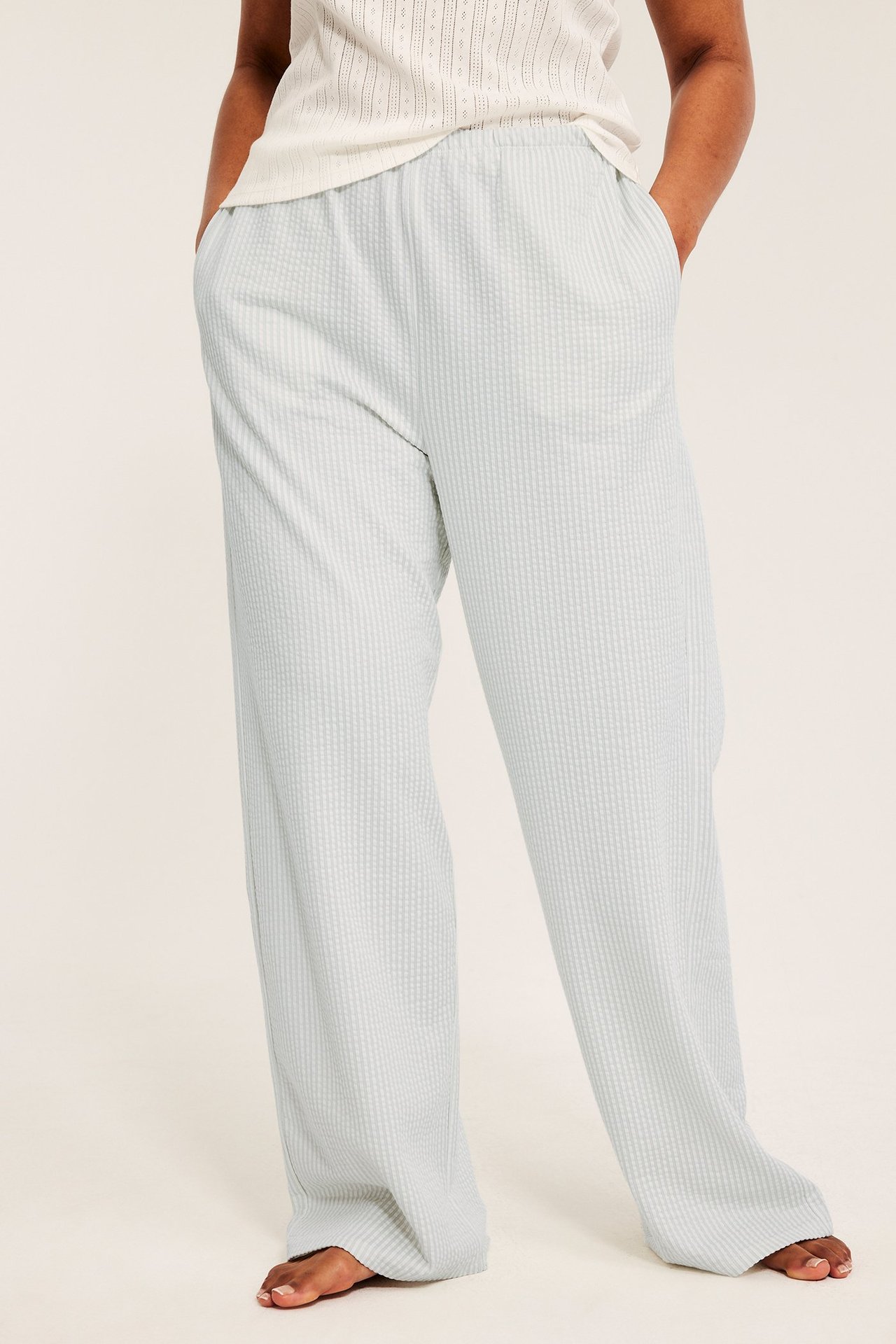 Framifrån: Kvinna i ljusgröna pyjamasbyxor med struktur, resår i midjan och sidfickor.