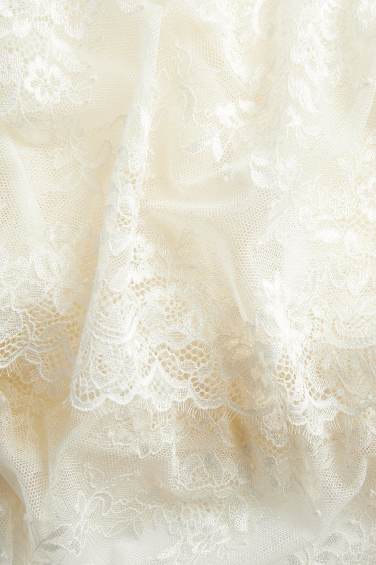 Zbliżenie na kremową koronkową tkaninę koszulki, ukazujące delikatne kwiatowe wzory i falbanki.