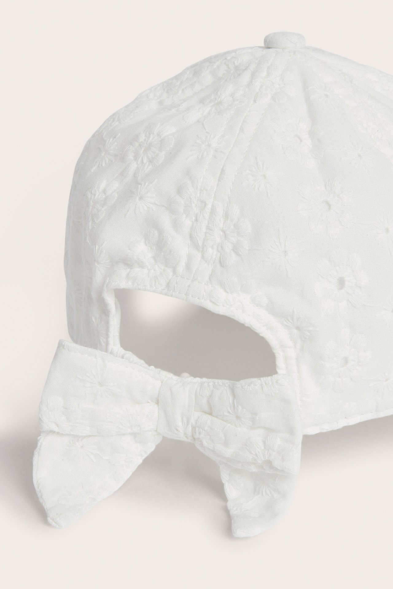Närbild, bakifrån av en offwhite barnkeps med blommig broderie anglaise och dekorativ rosett.