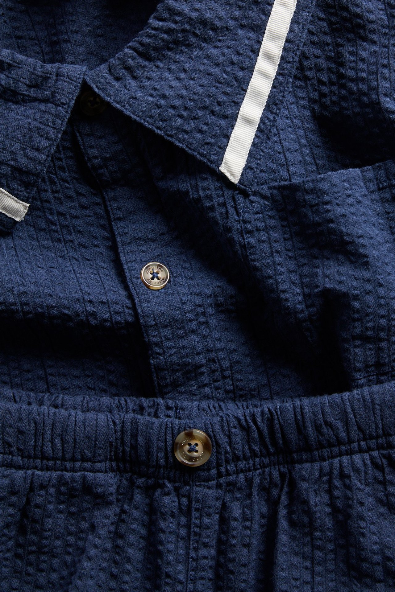 Zbliżenie na granatowy komplet dziecięcy seersucker: koszulę i szorty, z guzikami, kołnierzem i elastycznym pasem.