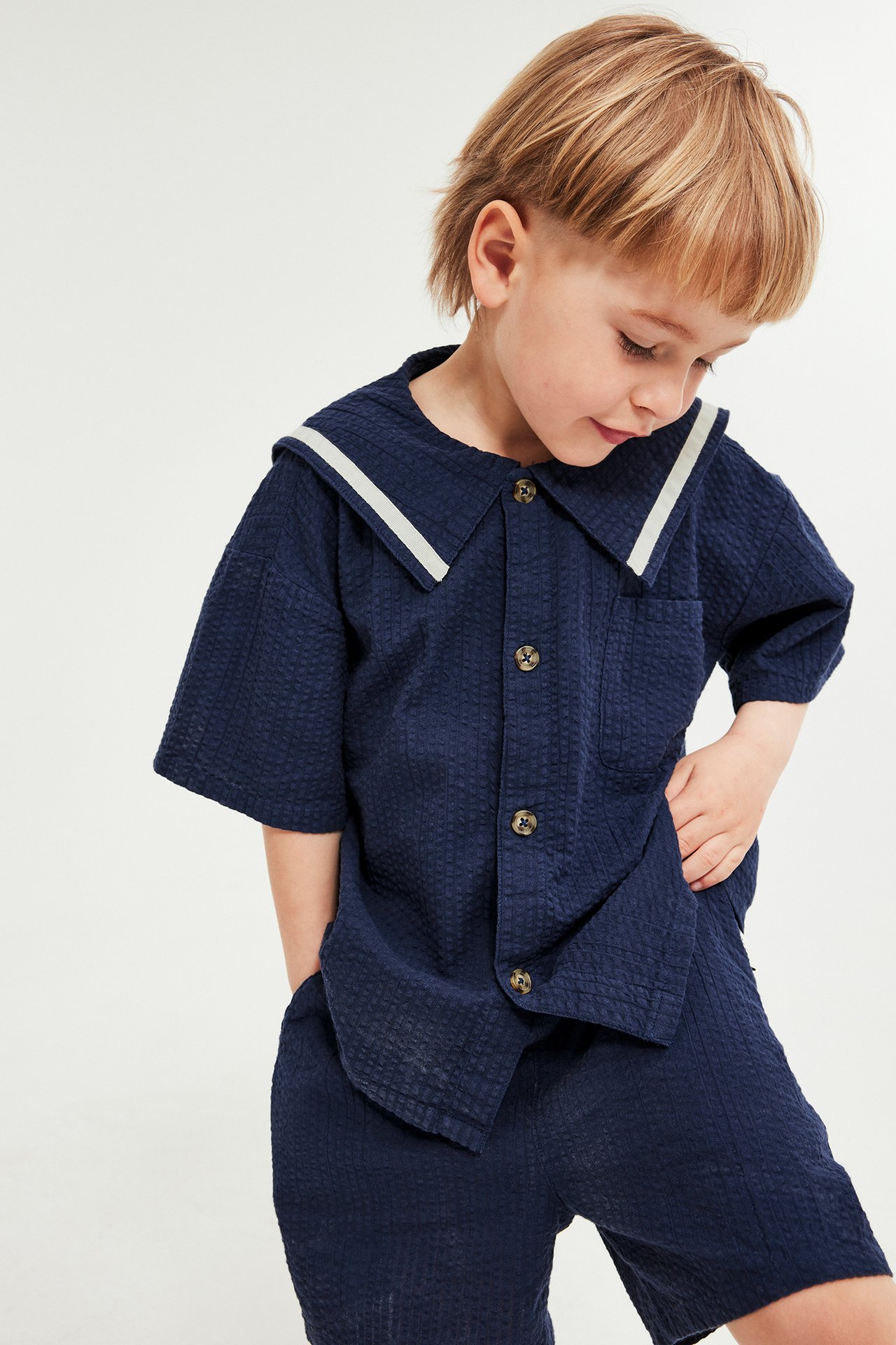 Frontvisning av et barn i marineblå seer-sucker kortermet skjorte med sjømannskrage og shorts.
