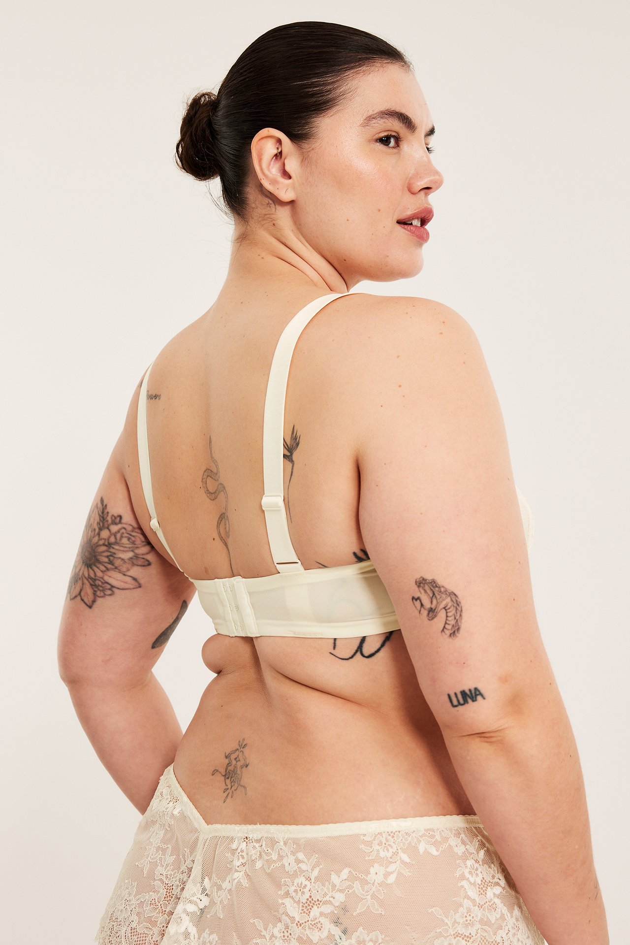 Naisen taka-sivukuva luonnonvalkoisissa kaarituellisissa rintaliiveissä ja yhteensopivissa pitsialushousuissa.