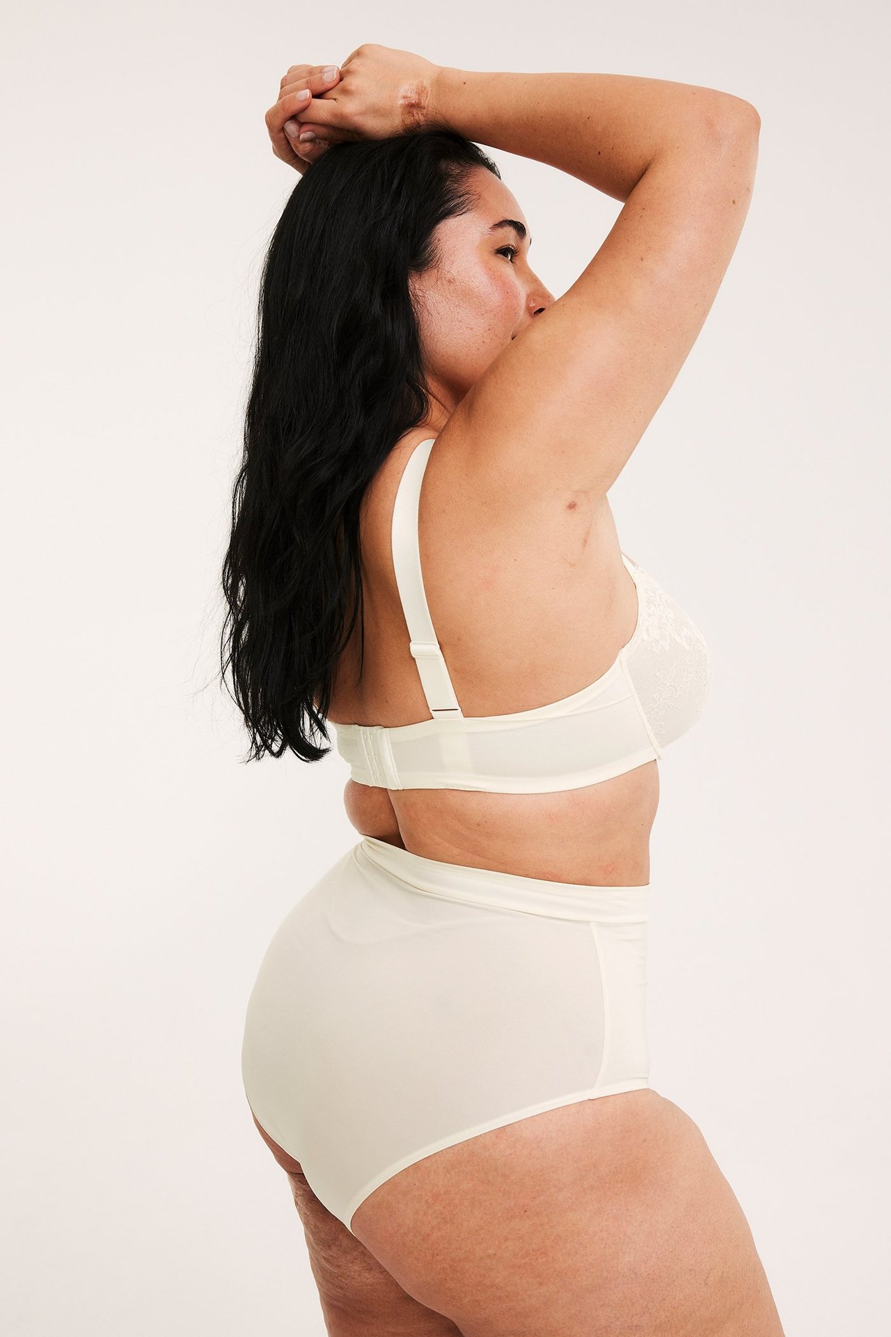 Widok z boku kobiety w beżowym koronkowym biustonoszu z fiszbinami i beżowych majtkach z wysokim stanem.