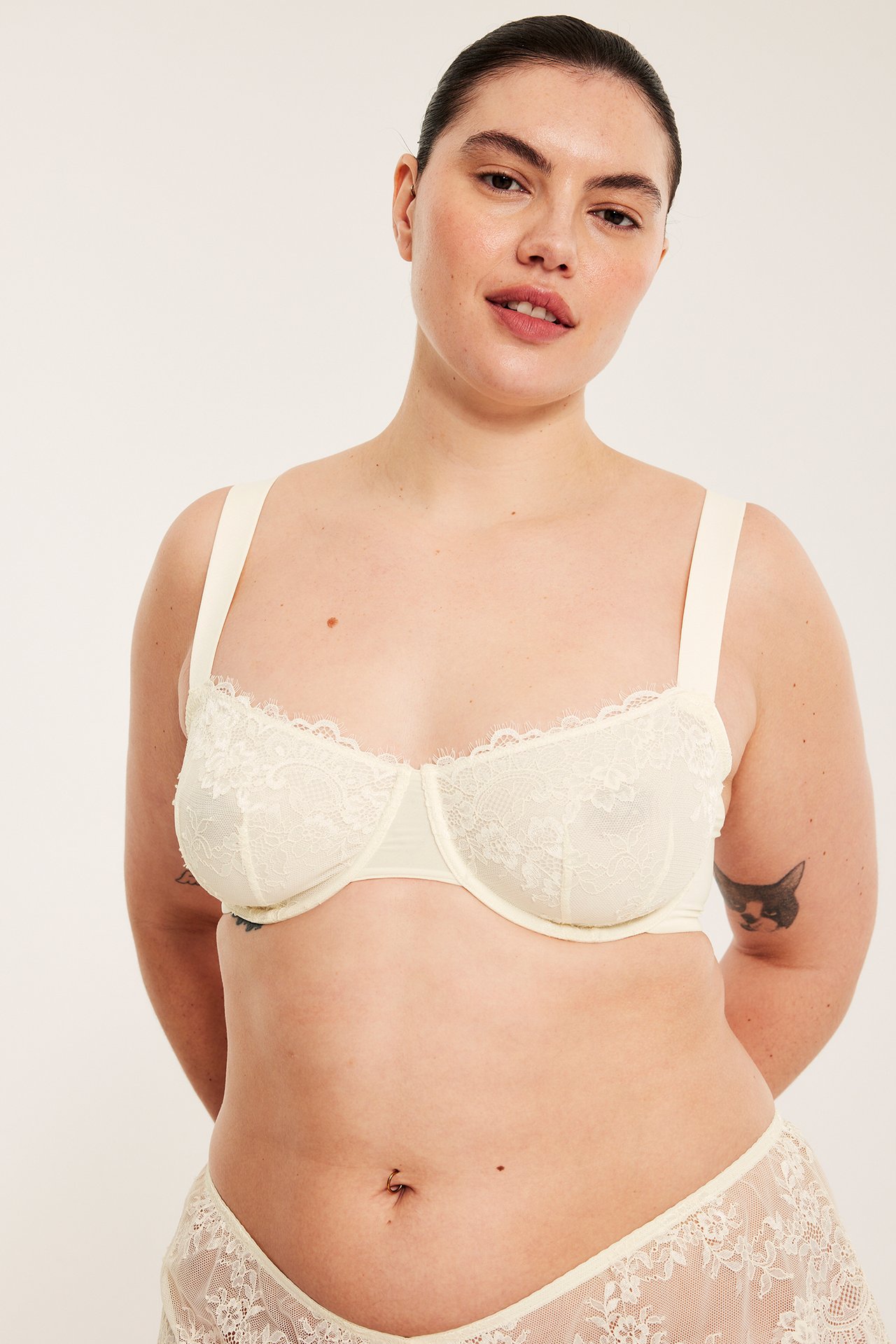 Framifrån, kvinna i offwhite bygel-bh i spets med balkongett-skärning och matchande spetsunderdel.