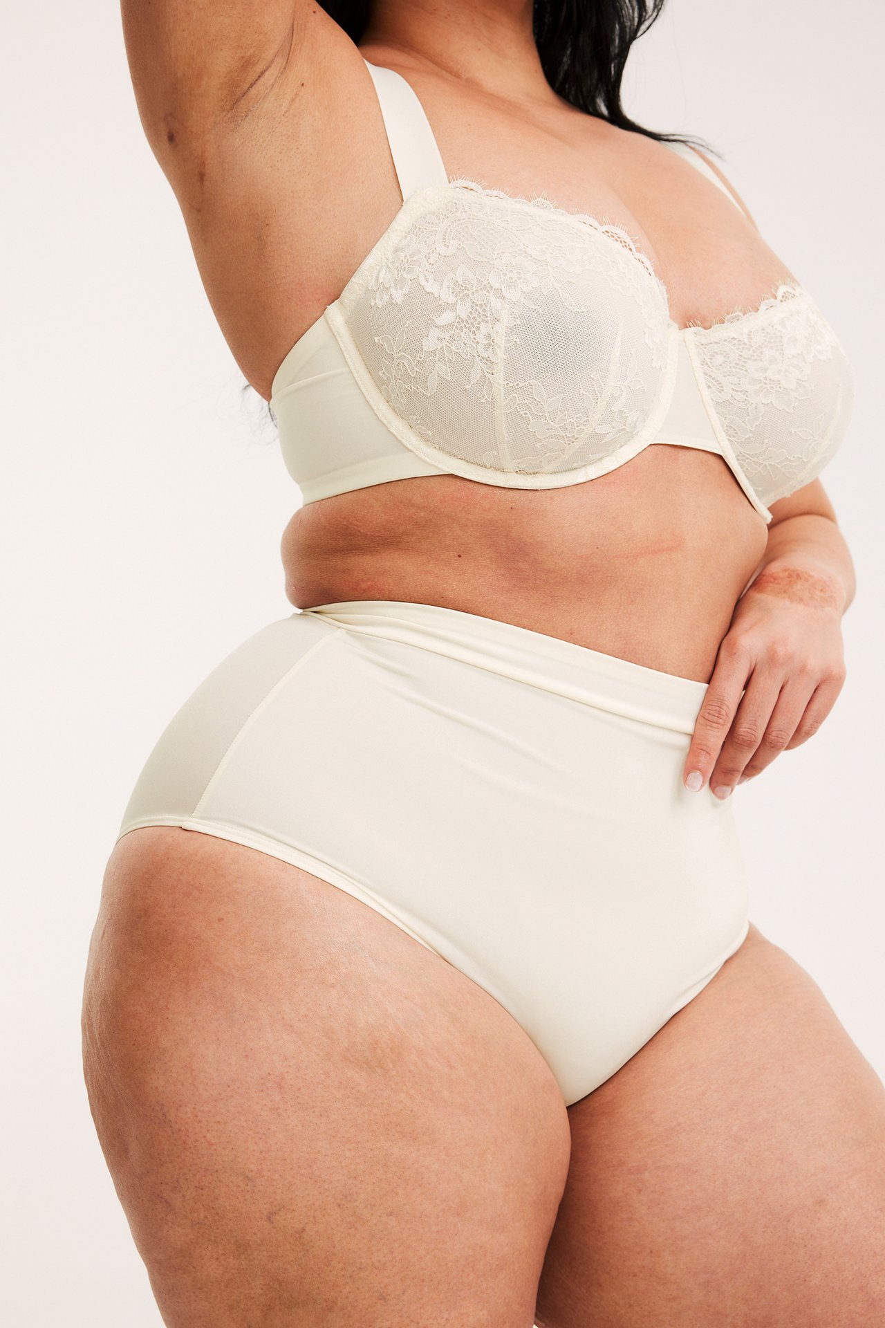 Widok z boku kobiety w biustonoszu z fiszbinami écru i pasujących majtkach z wysokim stanem.
