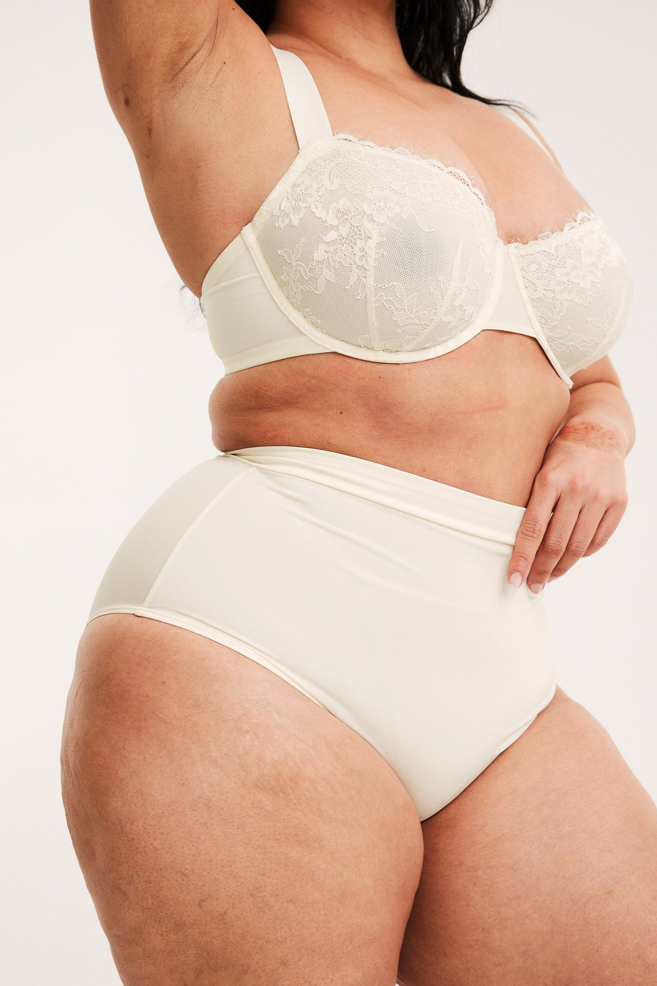 Sidovy av kvinna i offwhite bygel-bh i spets och matchande offwhite höga trosor.