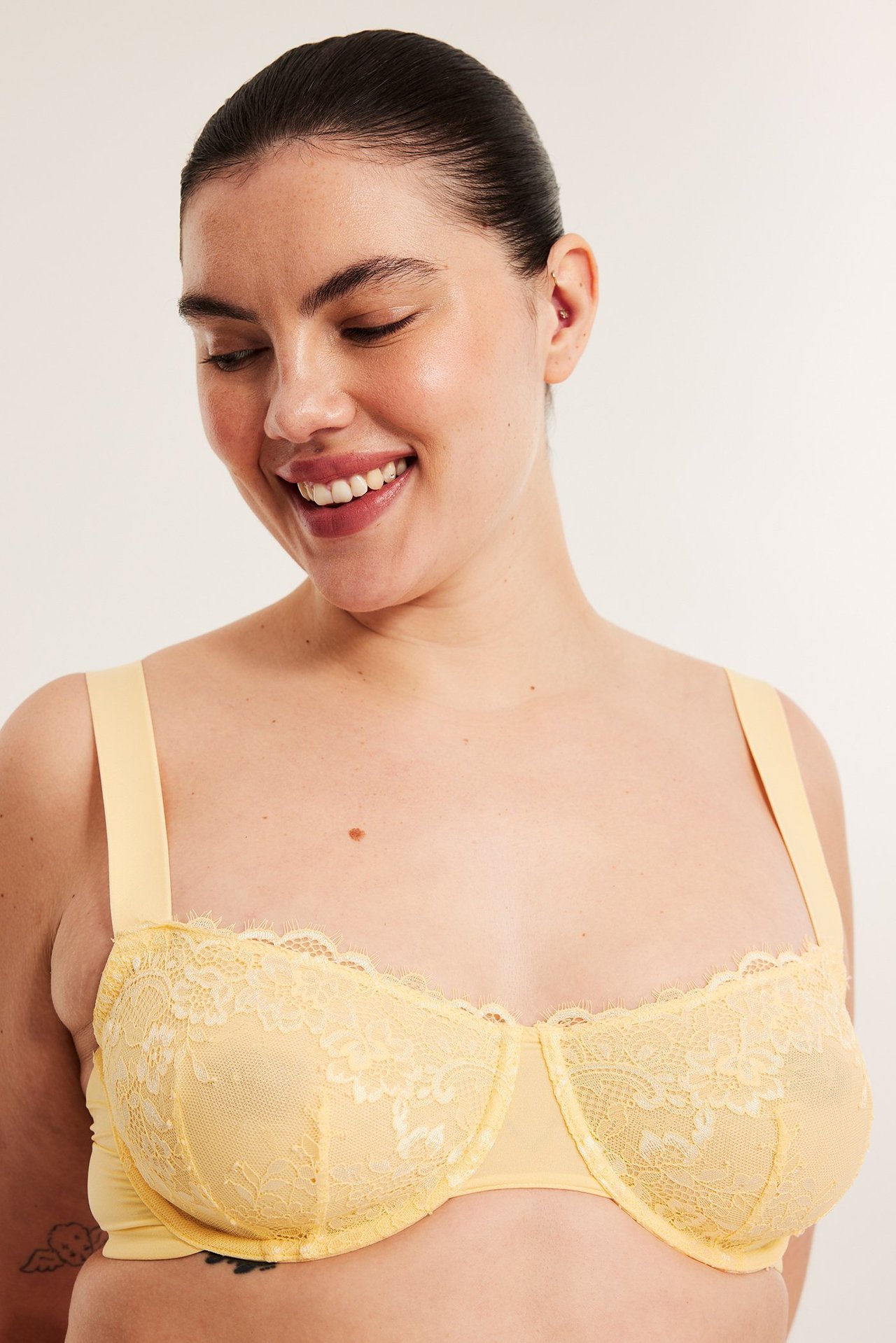Framsida av leende kvinna i ljusgul bygel-bh med spets och breda axelband.