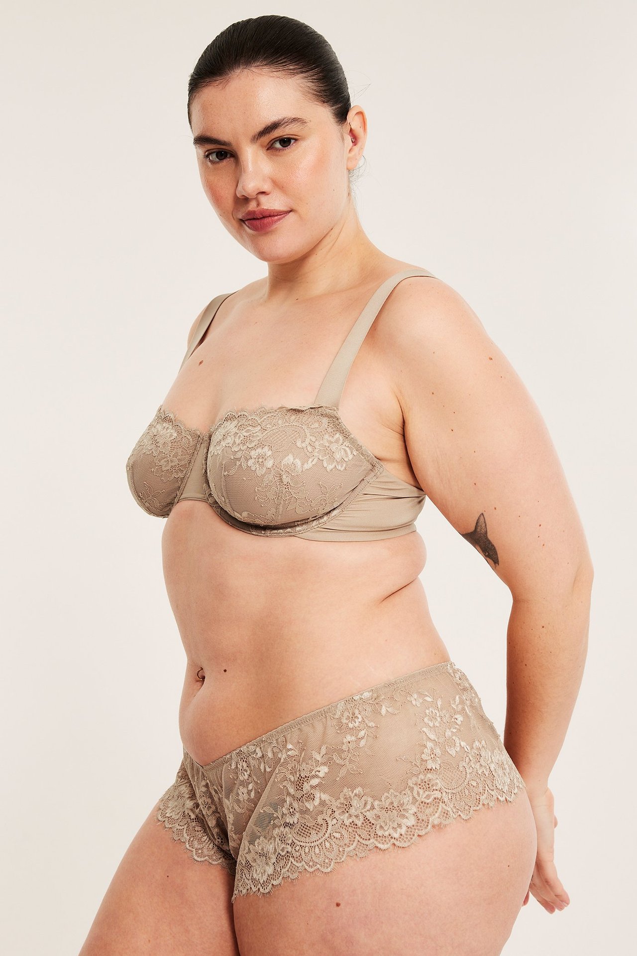 Sivukuva naisesta vaaleanruskeissa kaarituellisissa pitsiliiveissä ja yhteensopivissa pikkuhousuissa.