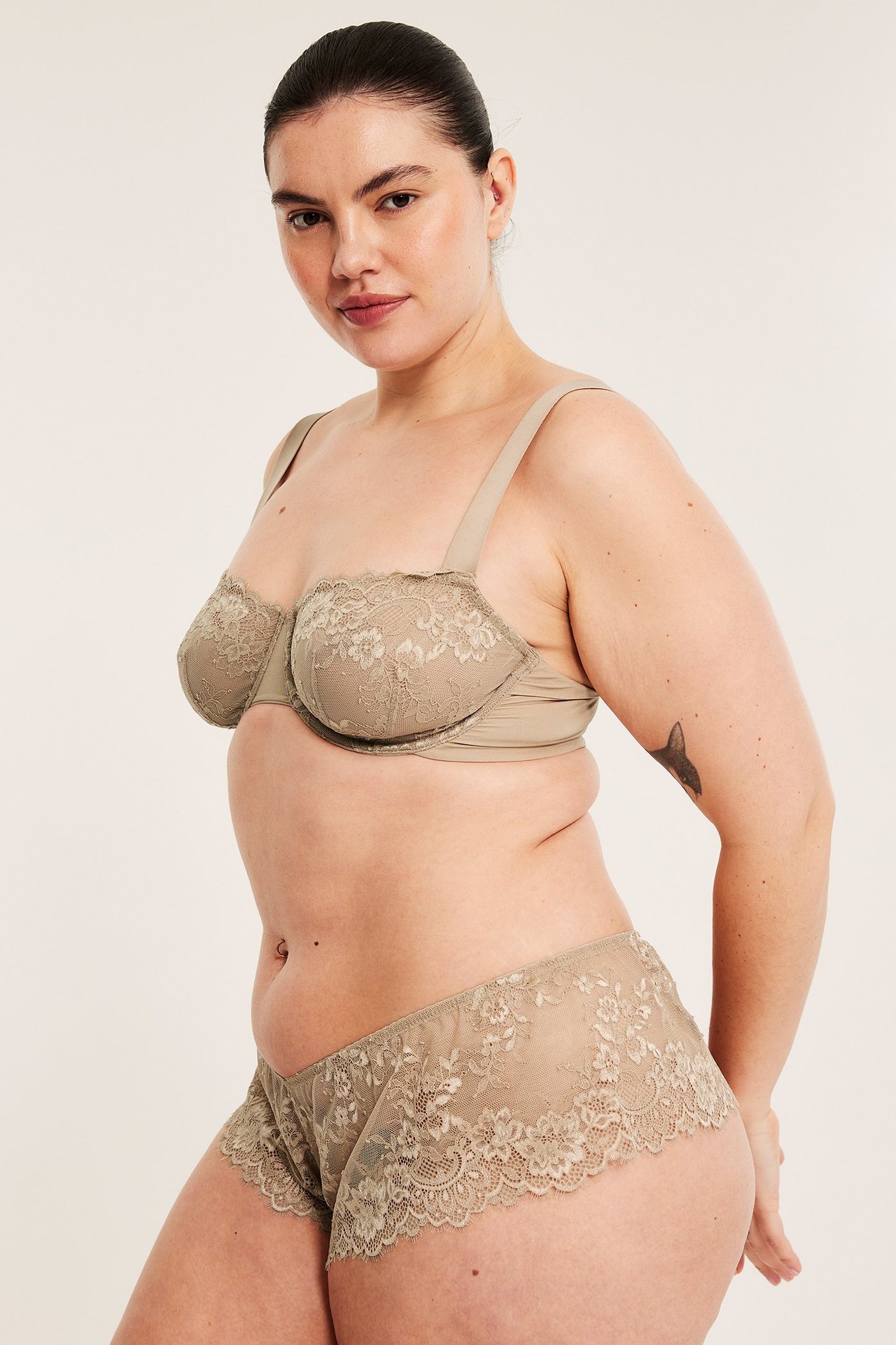 Sidovy av kvinna i ljusbrun bygel-bh med spets och matchande spetsshorts.